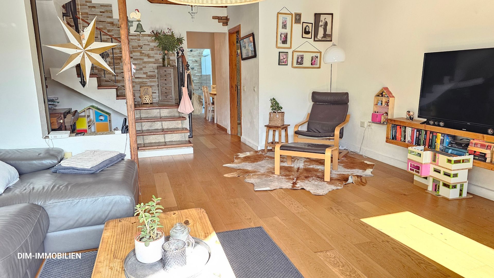 Ein Wohnzimmer mit Couch, Sessel, Tisch und Fernseher.