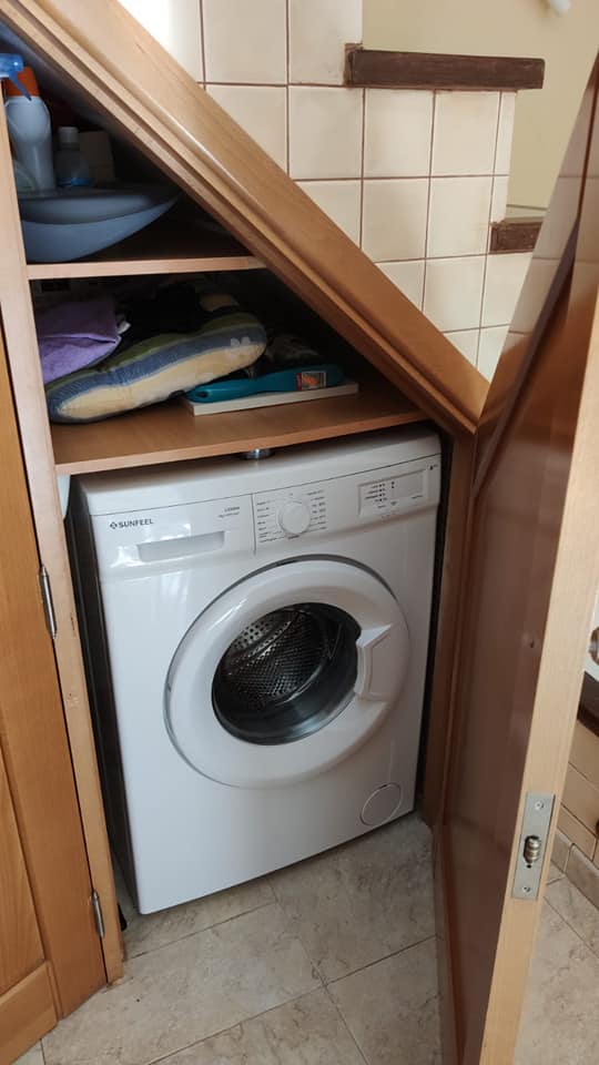 Eine Waschmaschine steht in einem Schrank unter einer Treppe.