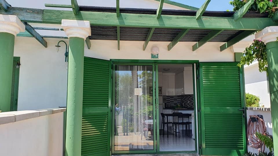 Die Vorderseite eines Hauses mit grünen Fensterläden und einer Pergola.