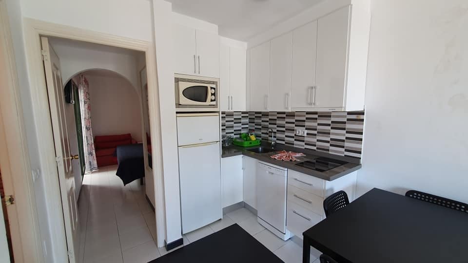 Eine Küche mit weißen Schränken, einem Kühlschrank, einer Mikrowelle und einem Tisch.