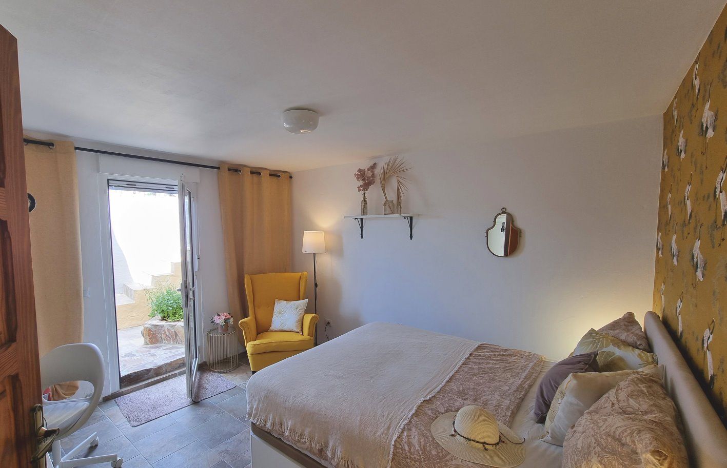 Ein Schlafzimmer mit Bett, Stuhl, Lampe, Spiegel und Glasschiebetüren.
