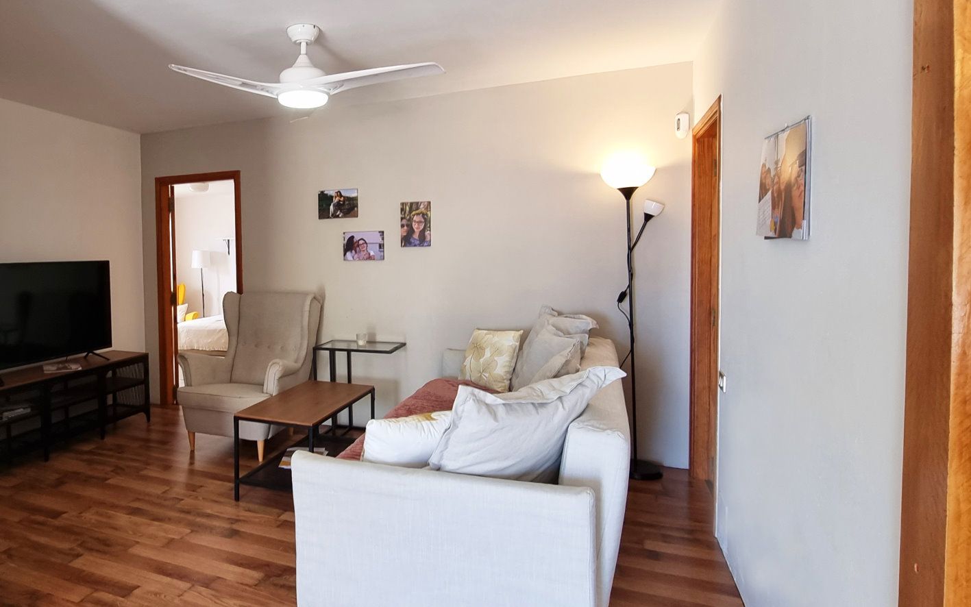 Ein Wohnzimmer mit Couch, Sessel, Tisch und Fernseher.