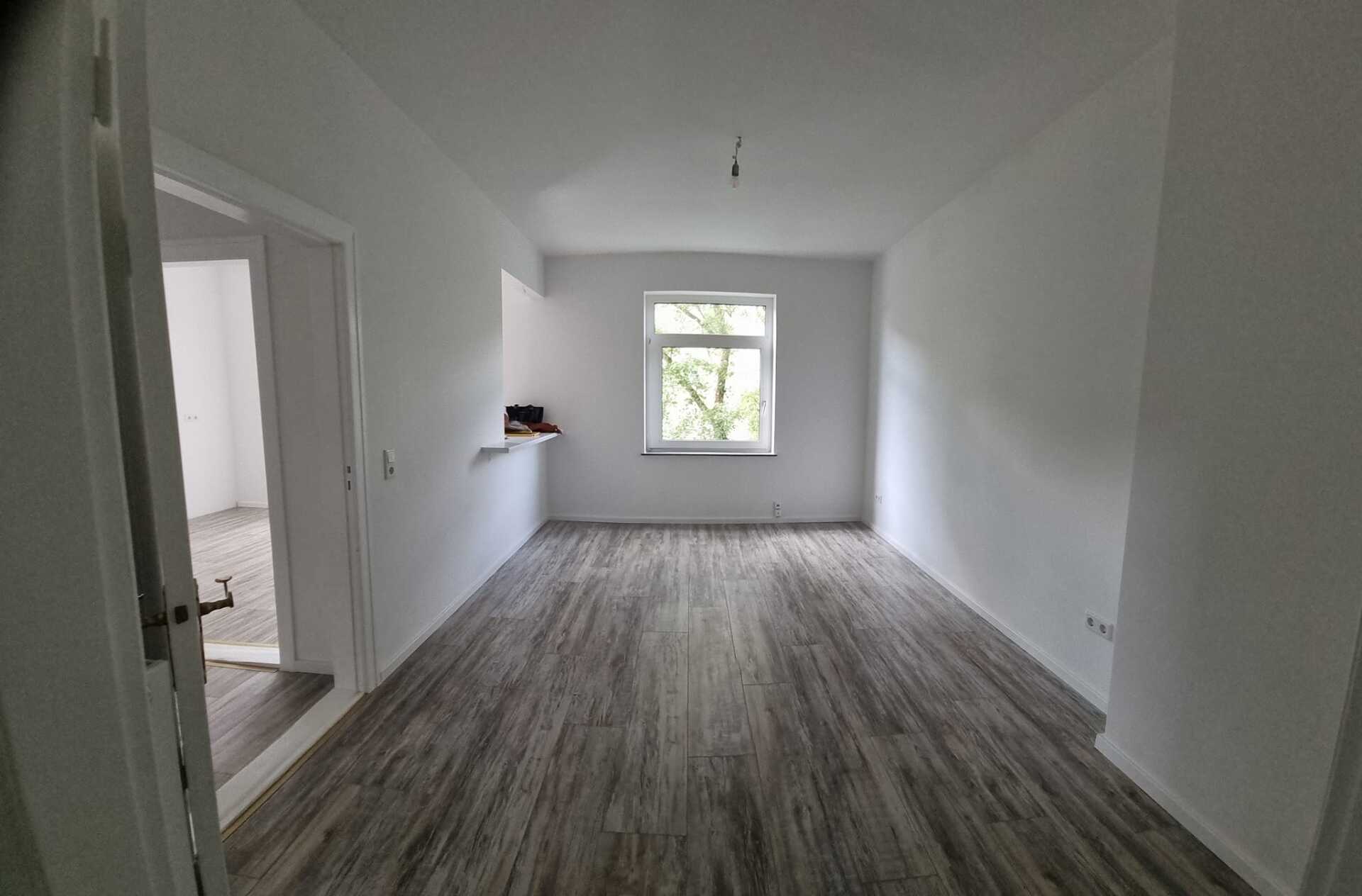 Ein leeres Wohnzimmer mit Holzboden und Fenster.
