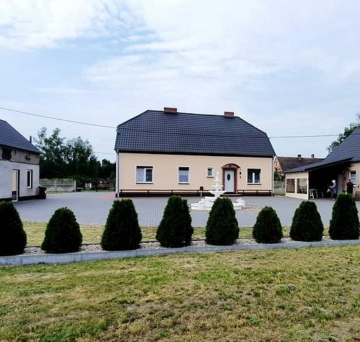 Ein großes Haus mit schwarzem Dach ist von Bäumen und Gras umgeben.