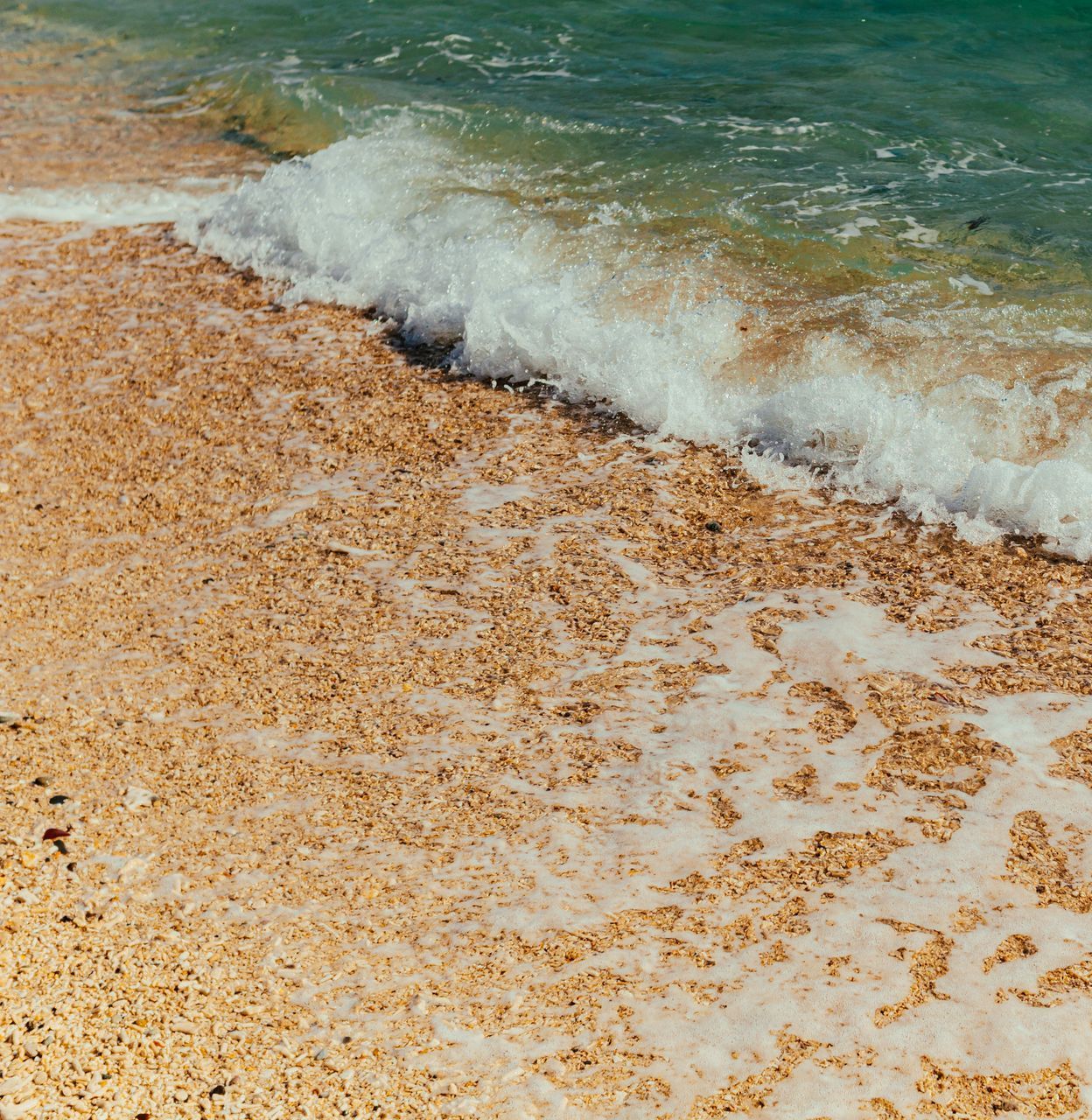 Eine Welle bricht an einem Sandstrand.
