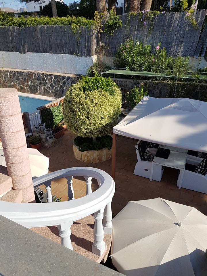 Ein Blick von einem Balkon auf eine Terrasse mit Sonnenschirmen und einem Pool.