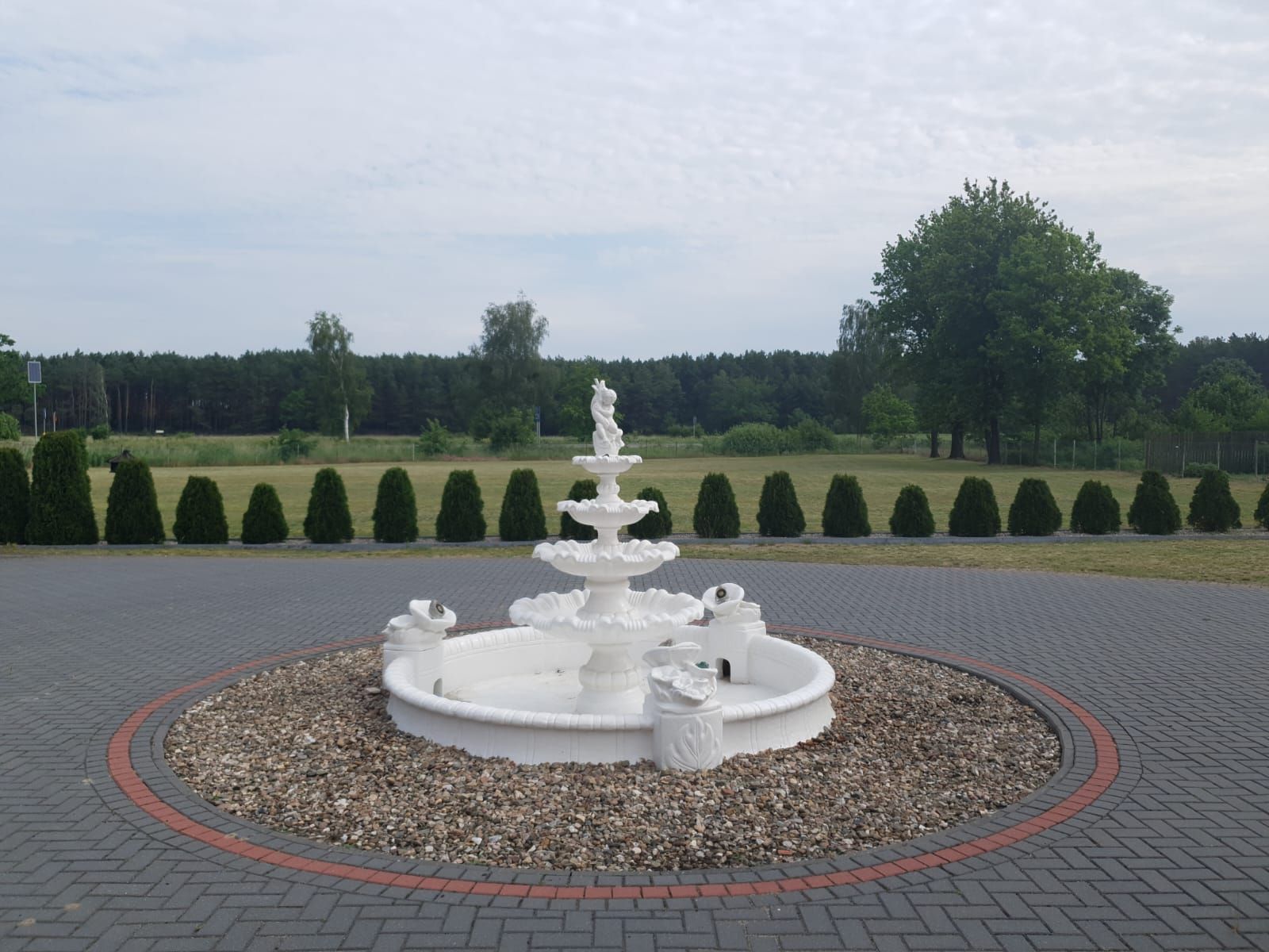 Ein weißer Brunnen steht in der Mitte einer gemauerten Auffahrt