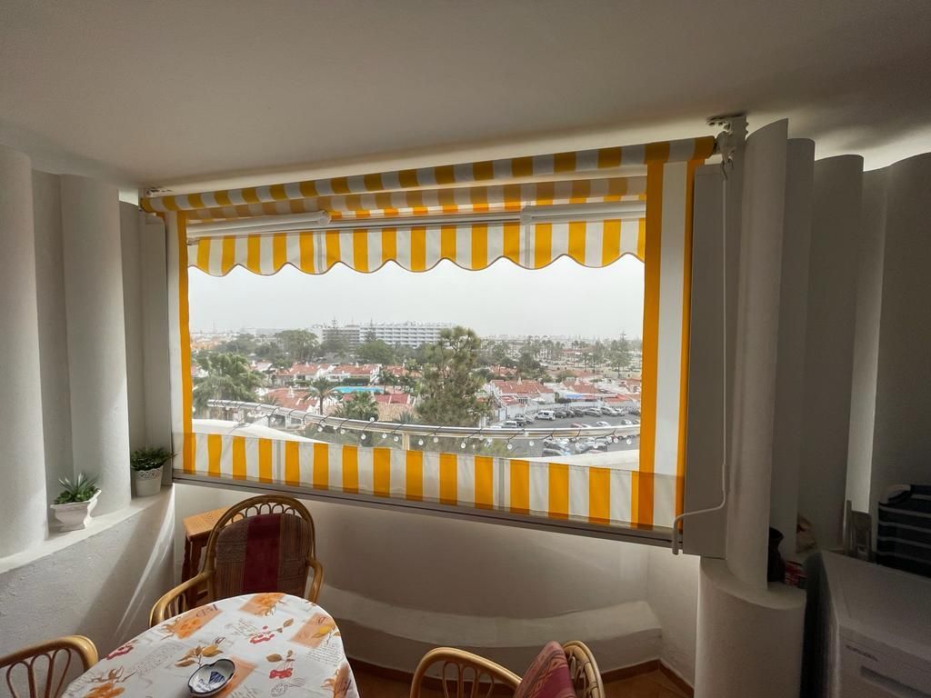 Ein Raum mit einem Tisch und Stühlen und einem Fenster mit einer gelb-weißen Markise