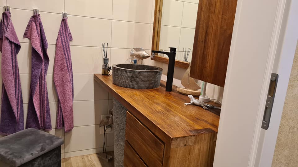 Ein Badezimmer mit Holzwaschtisch, Waschbecken, Spiegel und an der Wand hängenden Handtüchern.