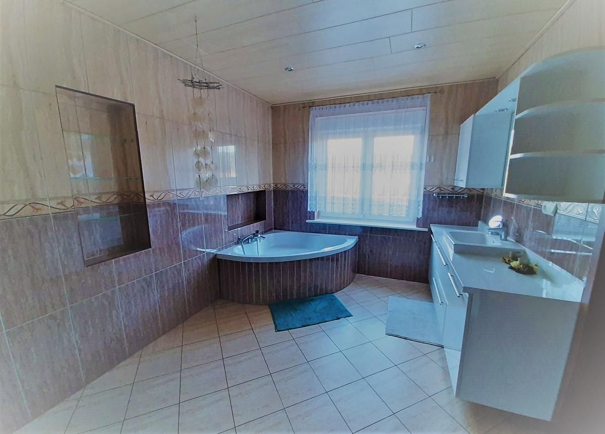 Ein Badezimmer mit Badewanne, Waschbecken, Schränken und Fenster.