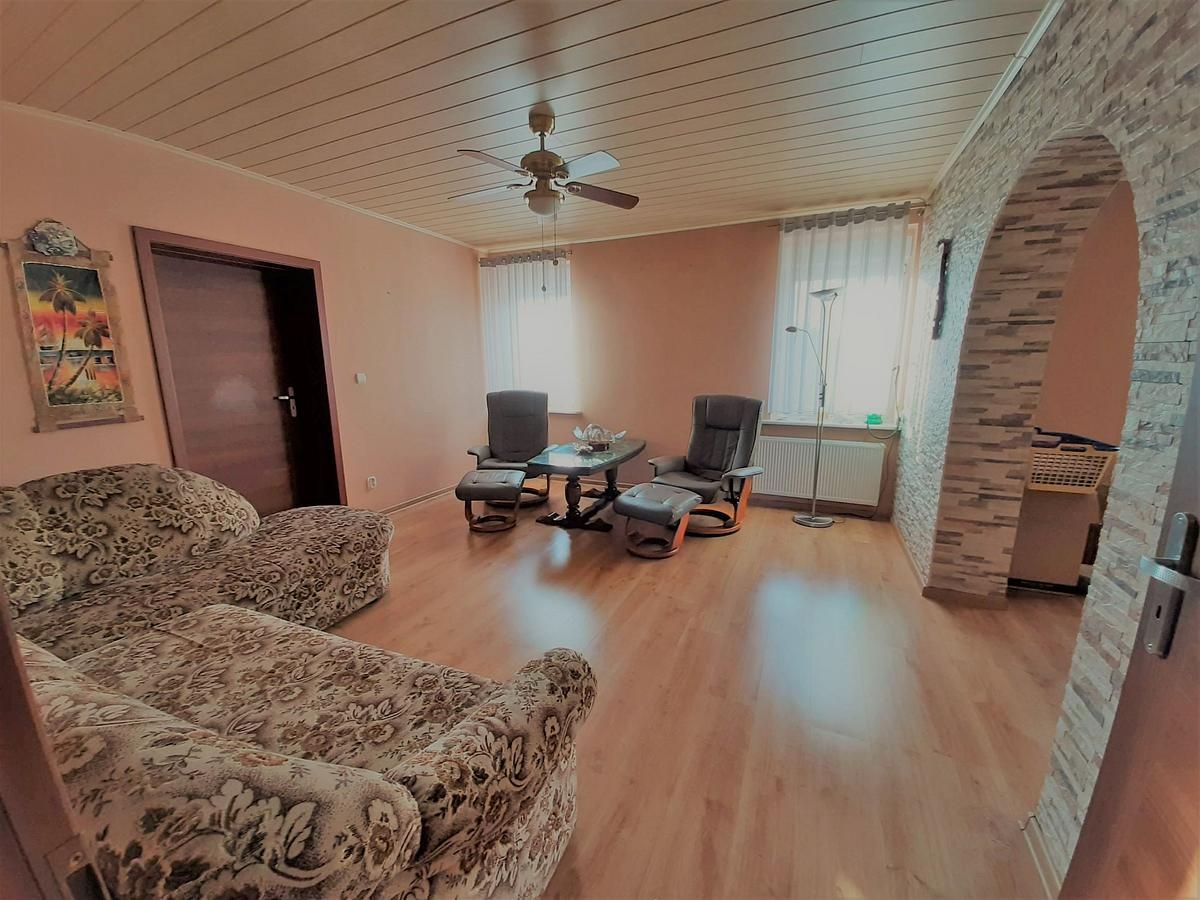 Ein Wohnzimmer mit einer Couch, zwei Stühlen, einem Tisch und einem Deckenventilator.