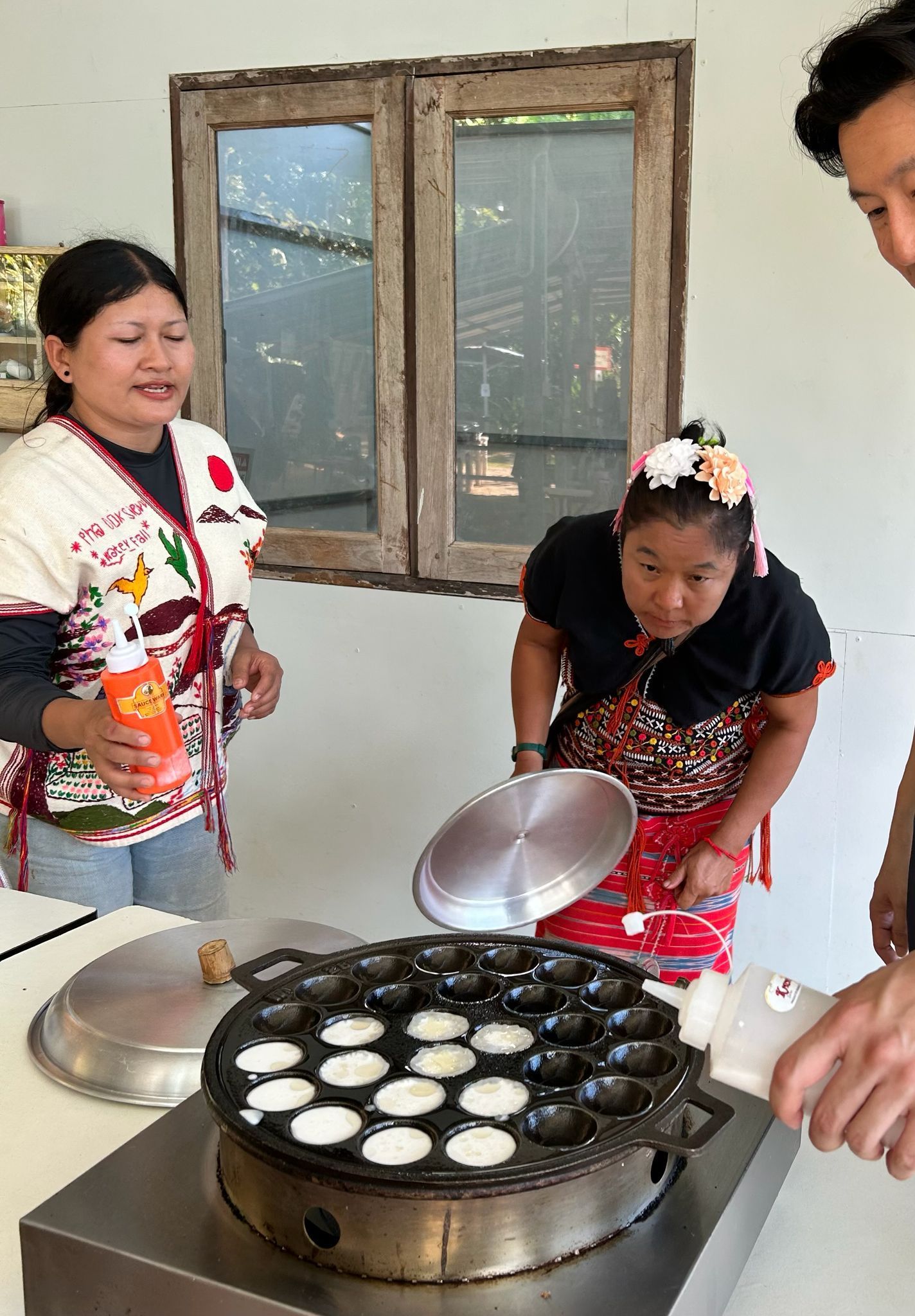 People cooking batter cakes on a round griddle indoors