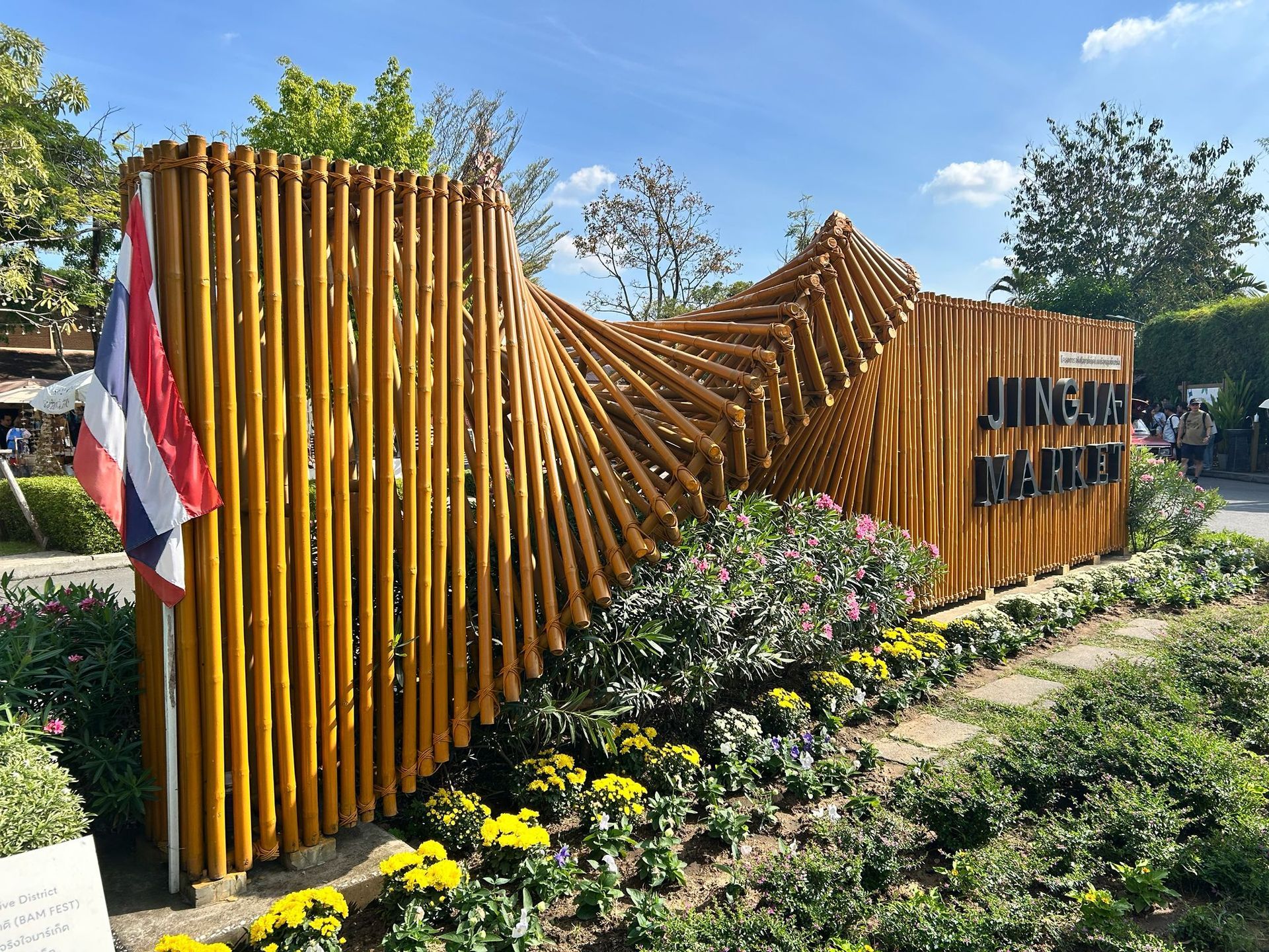 Decorative wooden installation with a Thai flag, flowers, and greenery in a sunny garden