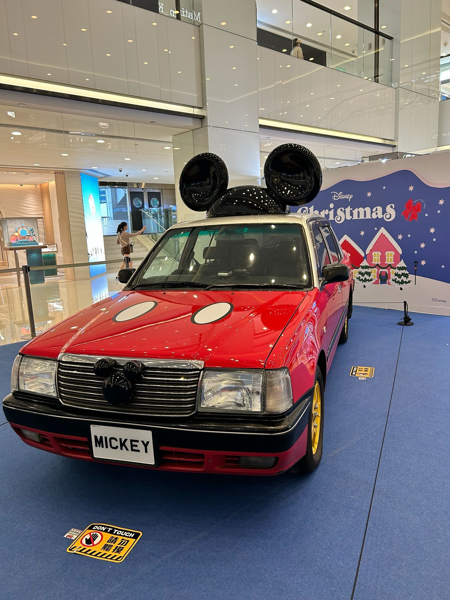 Red Mickey-themed car display with oversized black mouse ears in a mall lobby