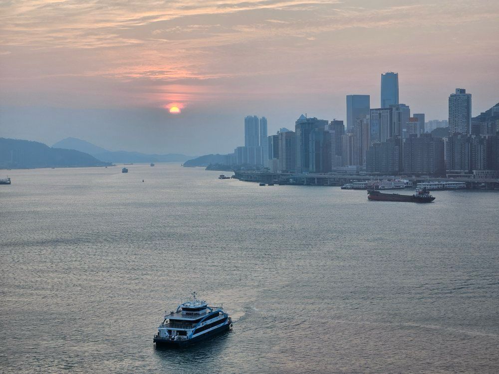 Sunset over a harbor with a city skyline and a ferry on calm water