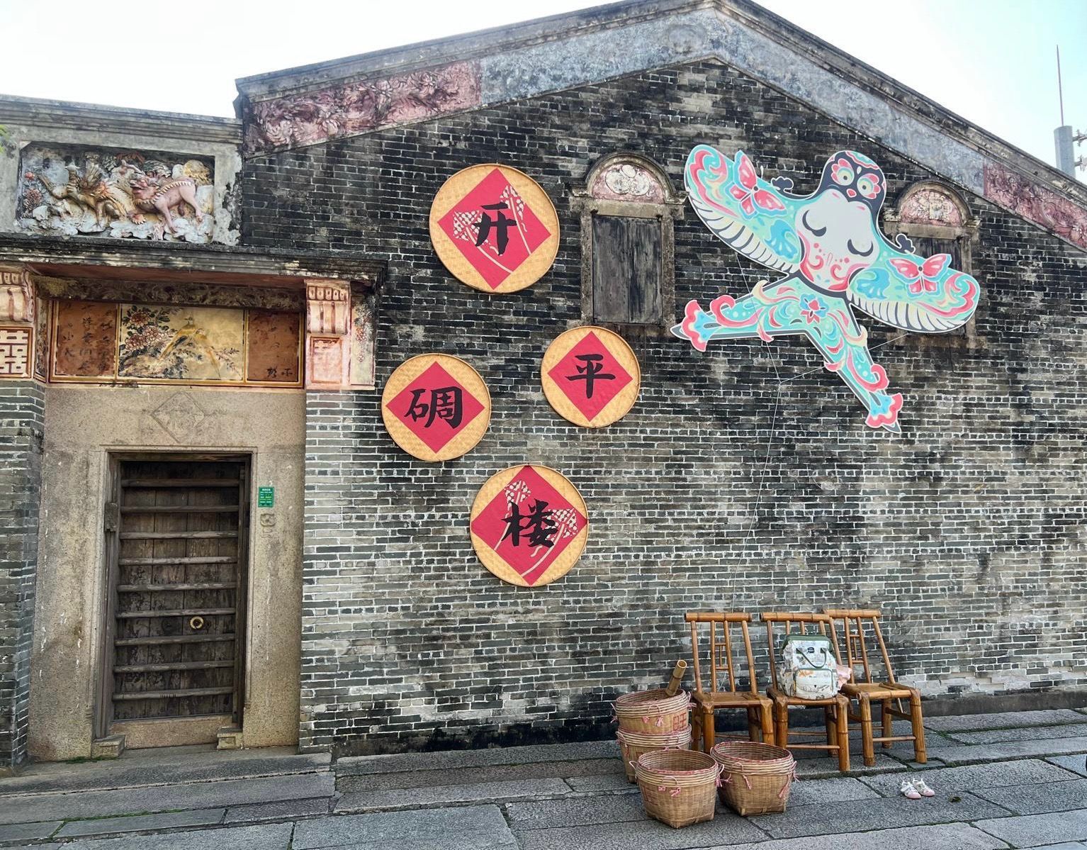Gray brick wall with colorful murals and red diamond Chinese characters above a wooden doorway