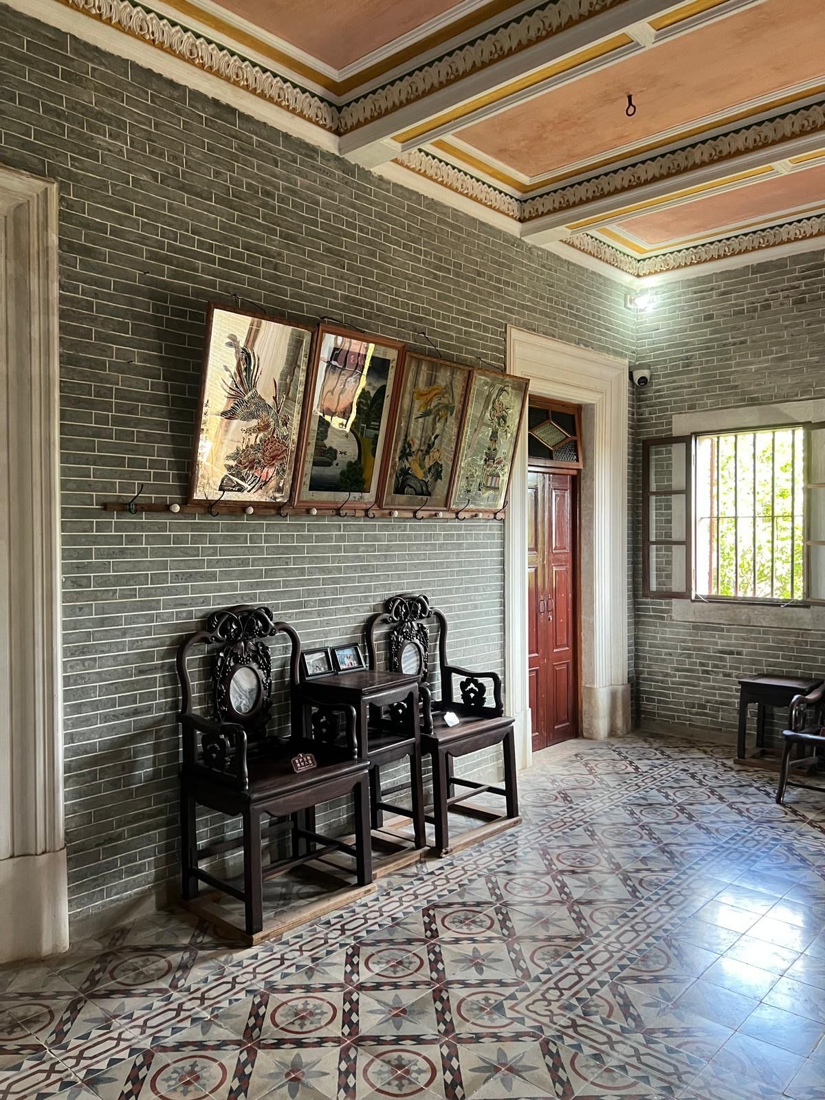 Small tiled living room with two black chairs, framed wall art, and a doorway beside a window.