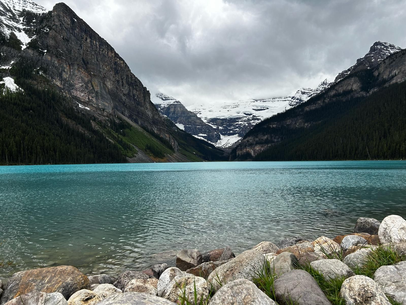 Turquoise mountain lake framed by rocky, forested peaks under a cloudy sky