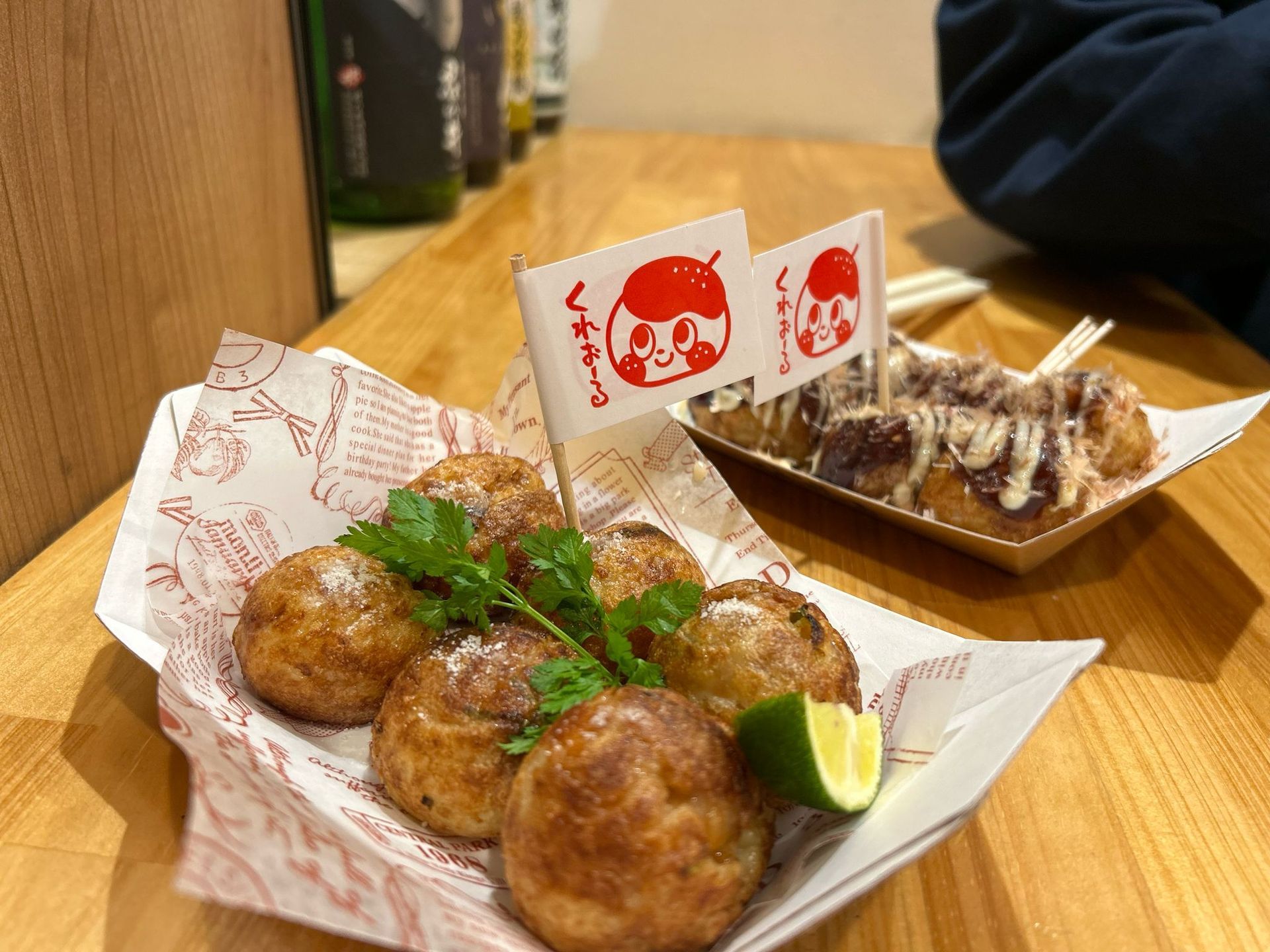 Takoyaki and grilled skewers on a wooden table with chopsticks and sauce cups