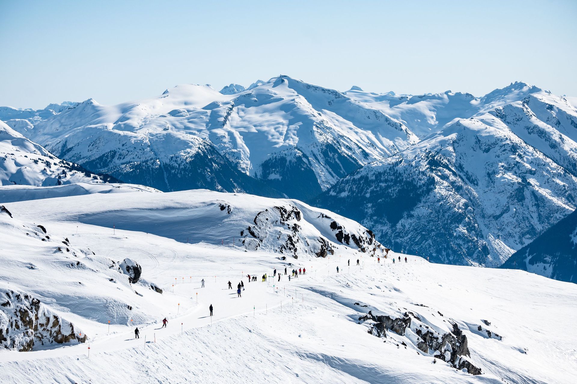 Snowy mountain range with skiers on a bright alpine slope under a clear blue sky