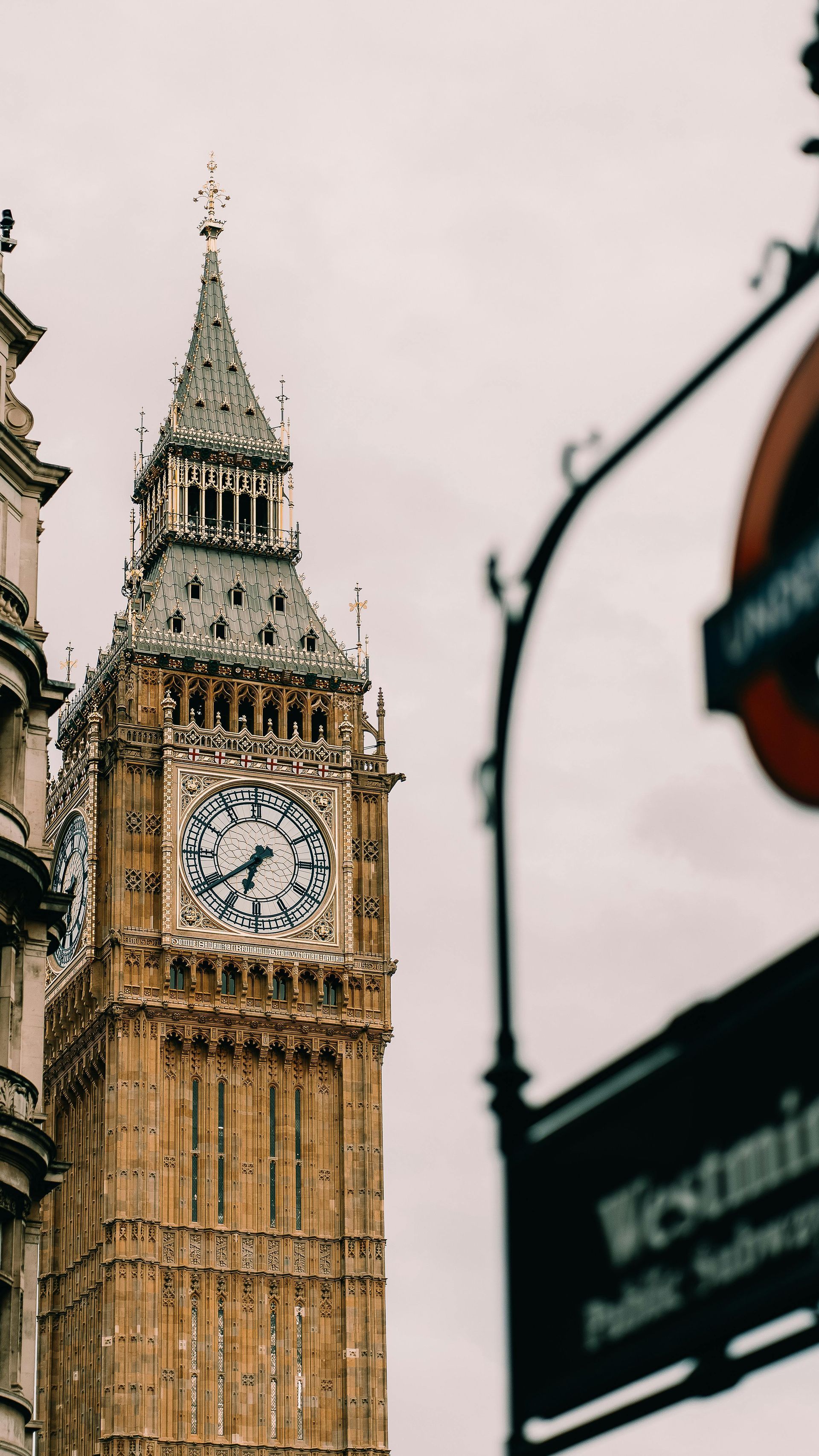 Big Ben clock tower in London against a pale sky, with a blurred street sign in the foreground