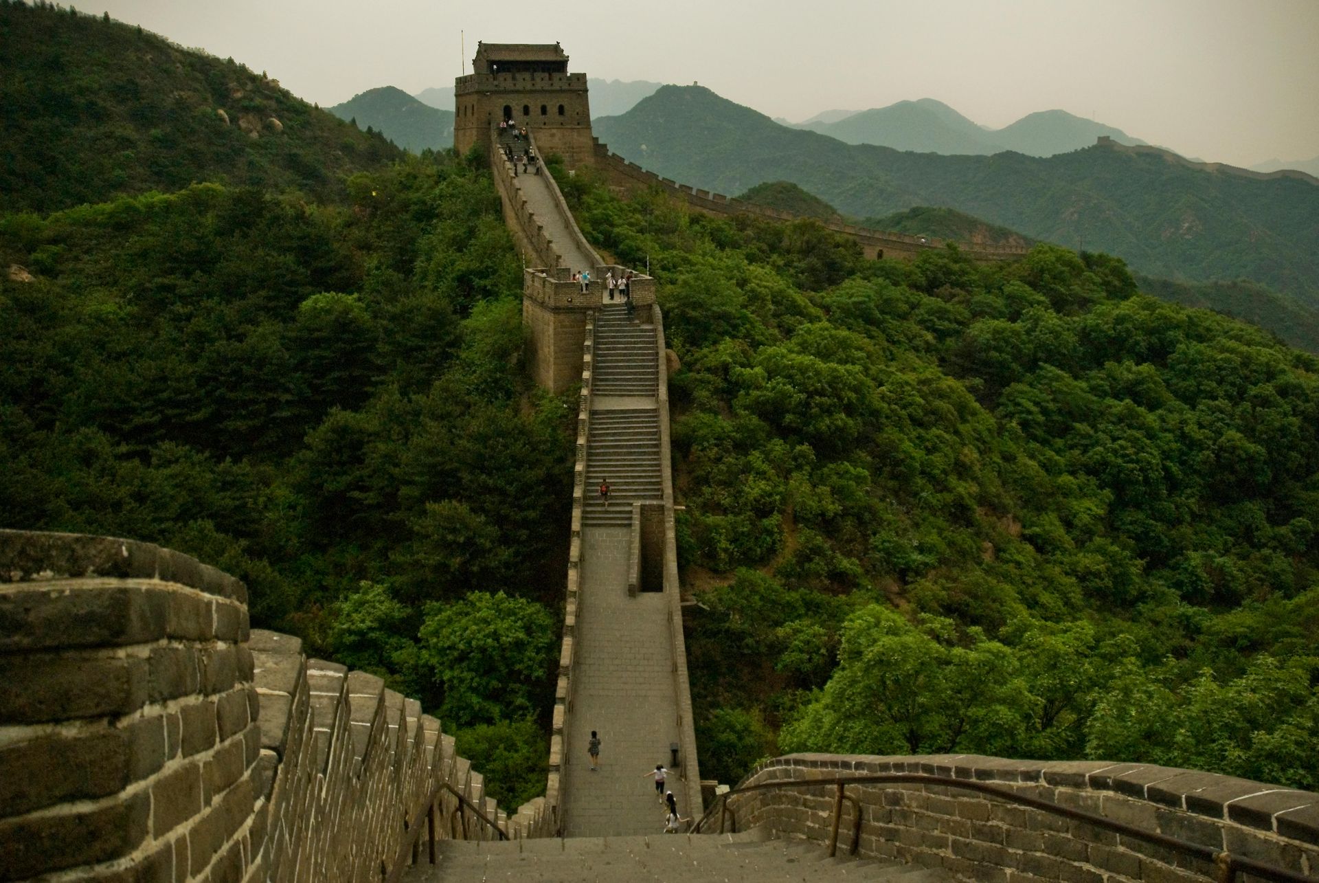 The Great Wall of China winding through green mountains under a hazy sky.