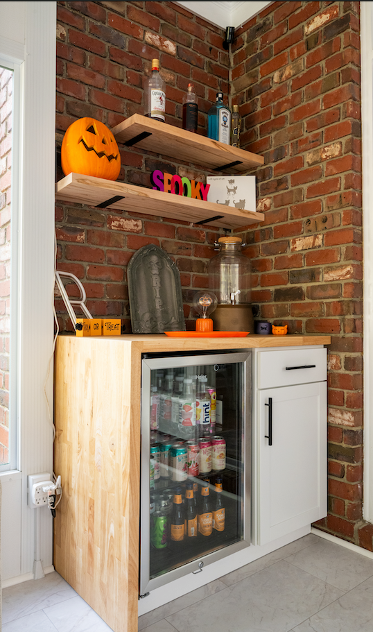 Small brick alcove with white cabinet, glass cooler, shelves, and pumpkin decor.