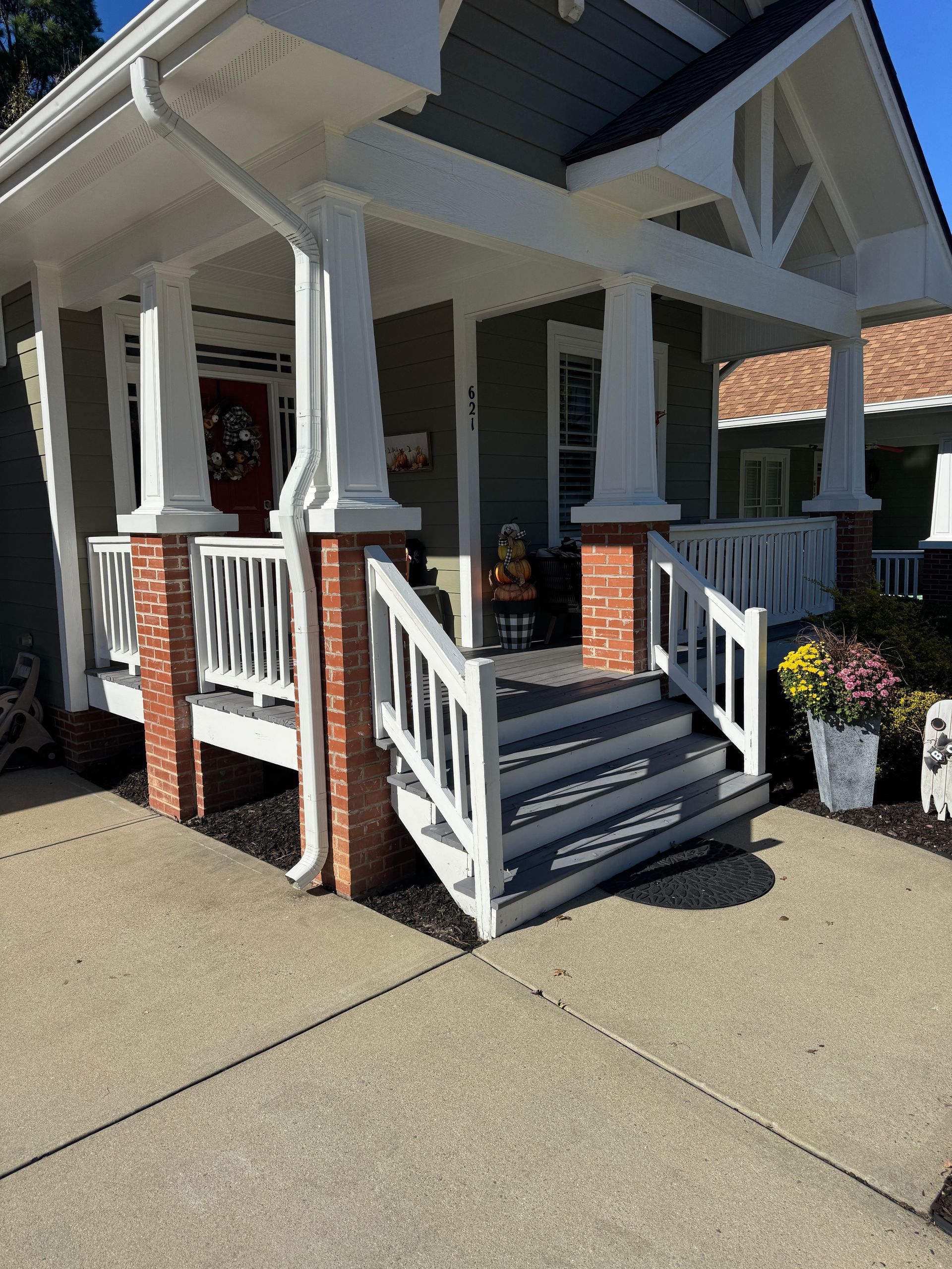 Front porch with white railings and steps on a brick house, viewed from the sidewalk.