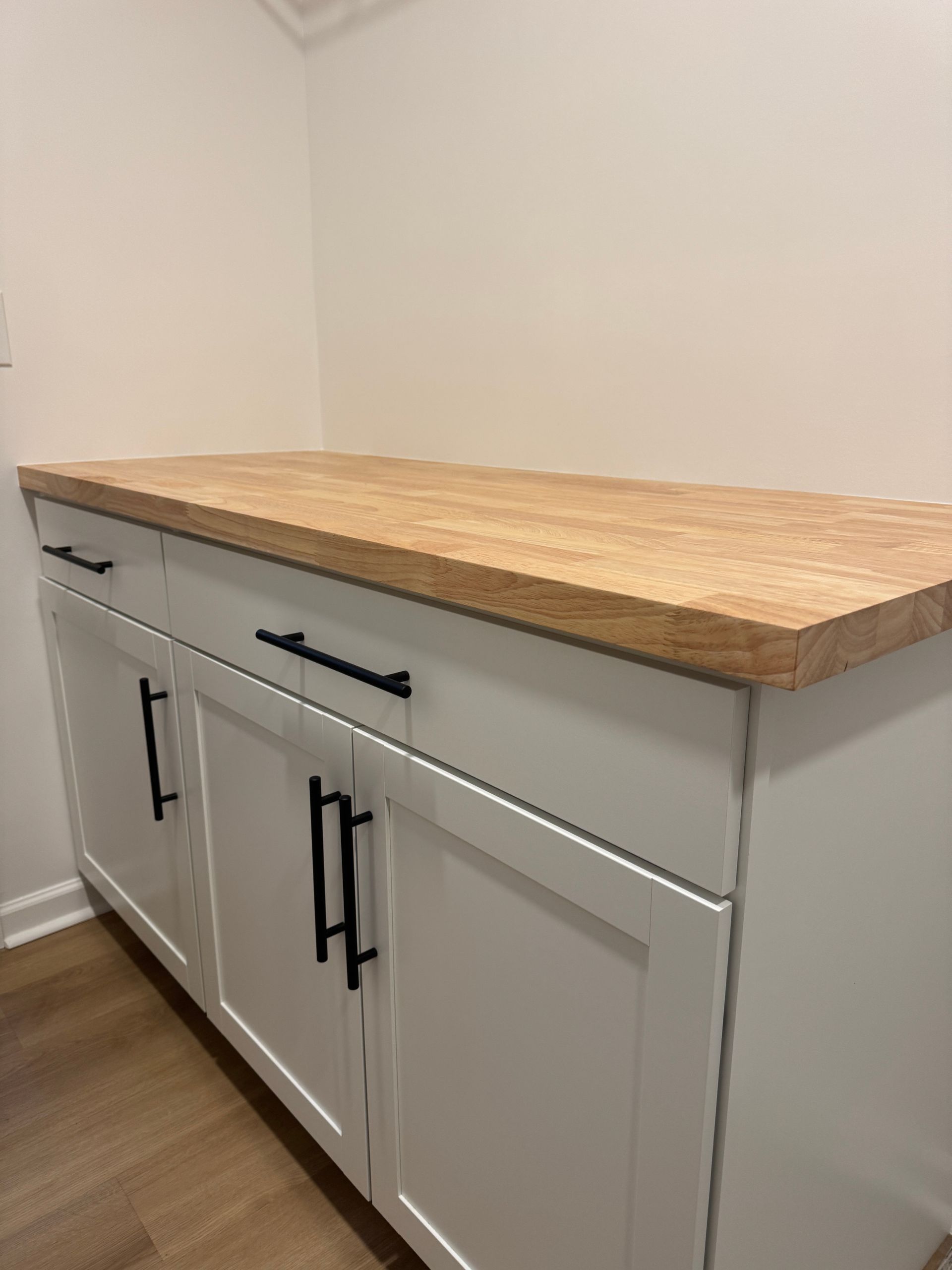White built-in cabinet with black handles and a wood countertop along a wall.