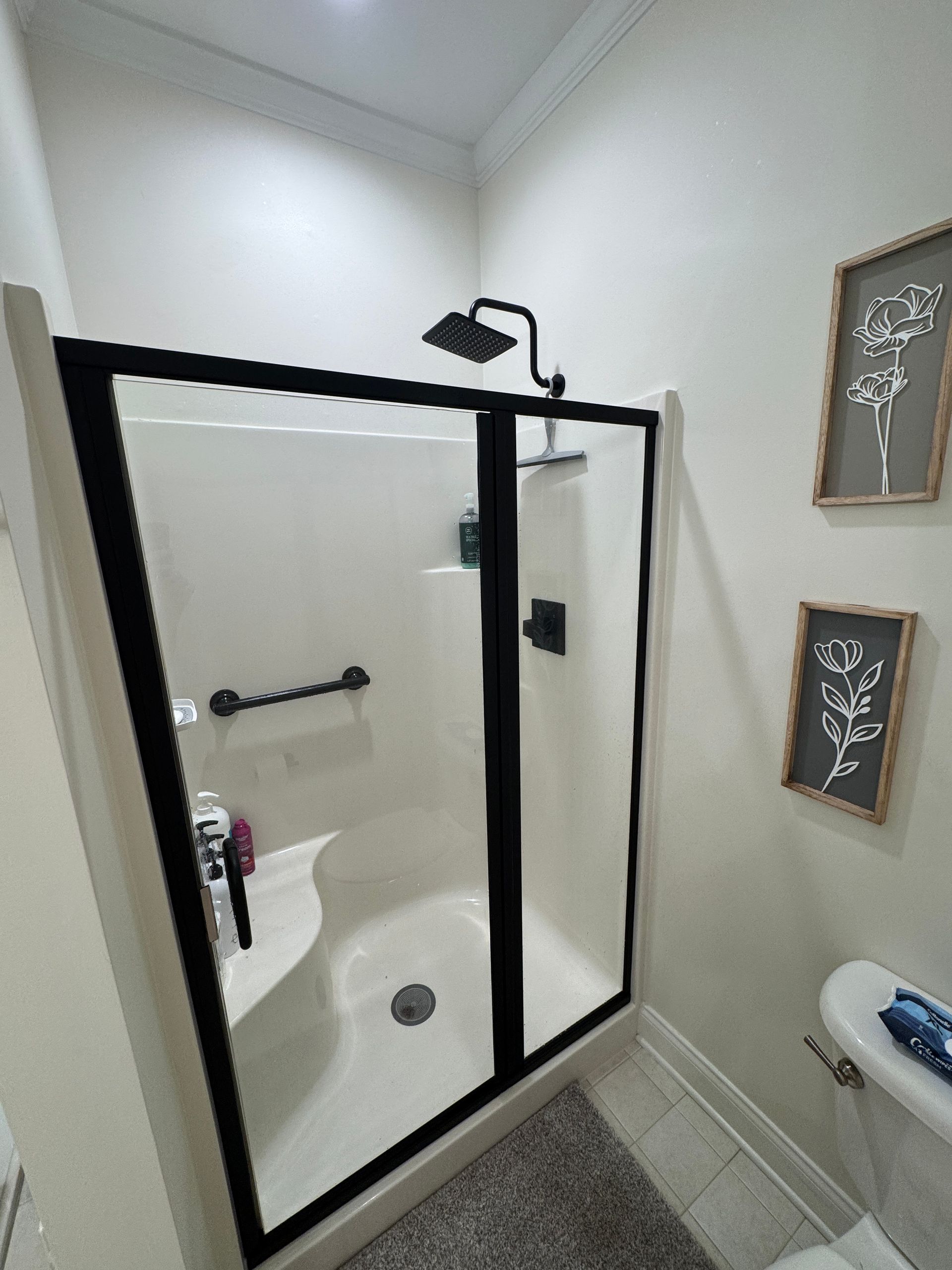 Small bathroom with a glass-enclosed shower, white walls, and two framed floral wall decorations.
