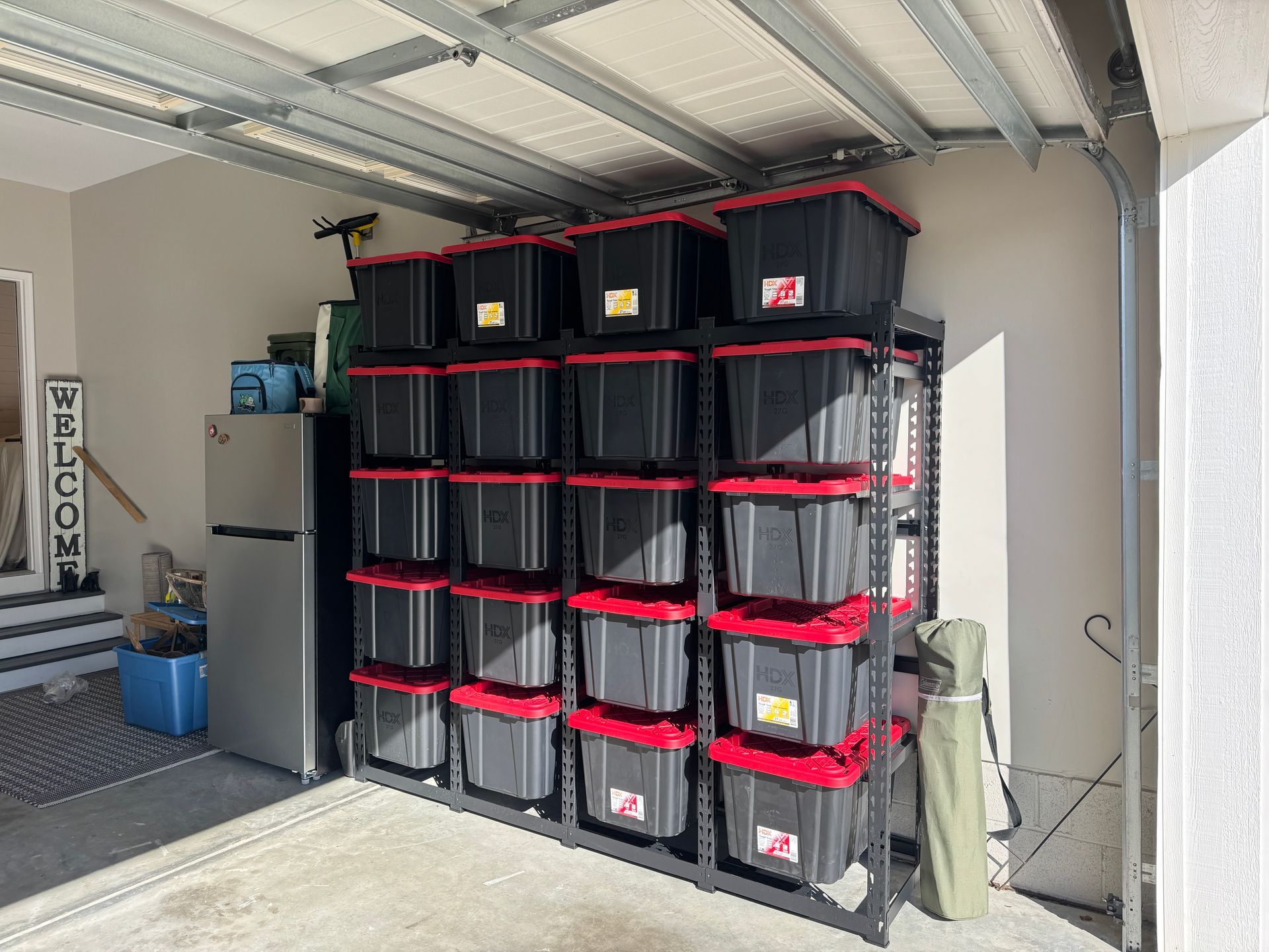 Garage storage shelves with stacked black bins and red lids under a metal roof