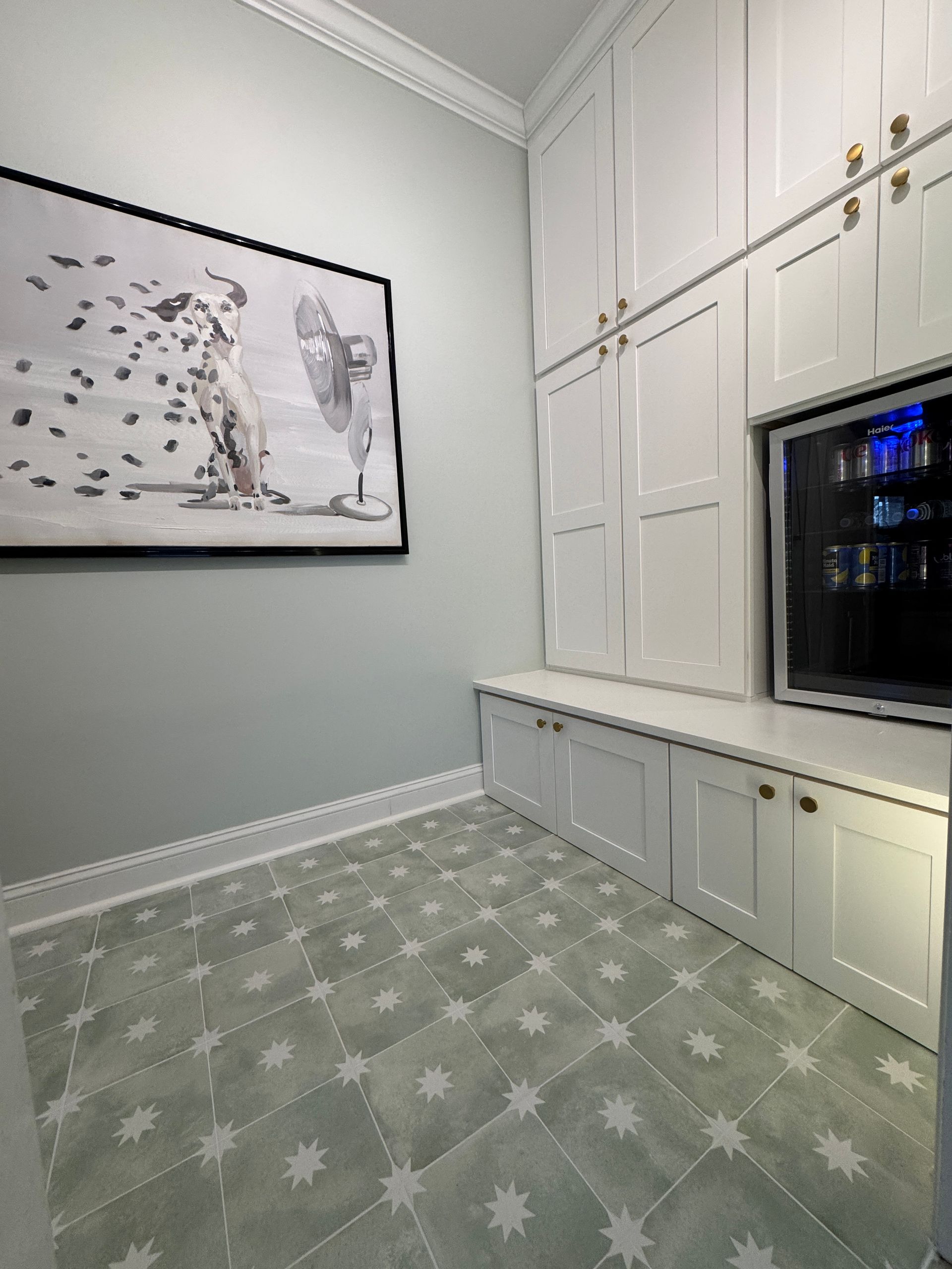 White built-in cabinets and bench along a wall in a bright room with patterned green carpet and framed art.