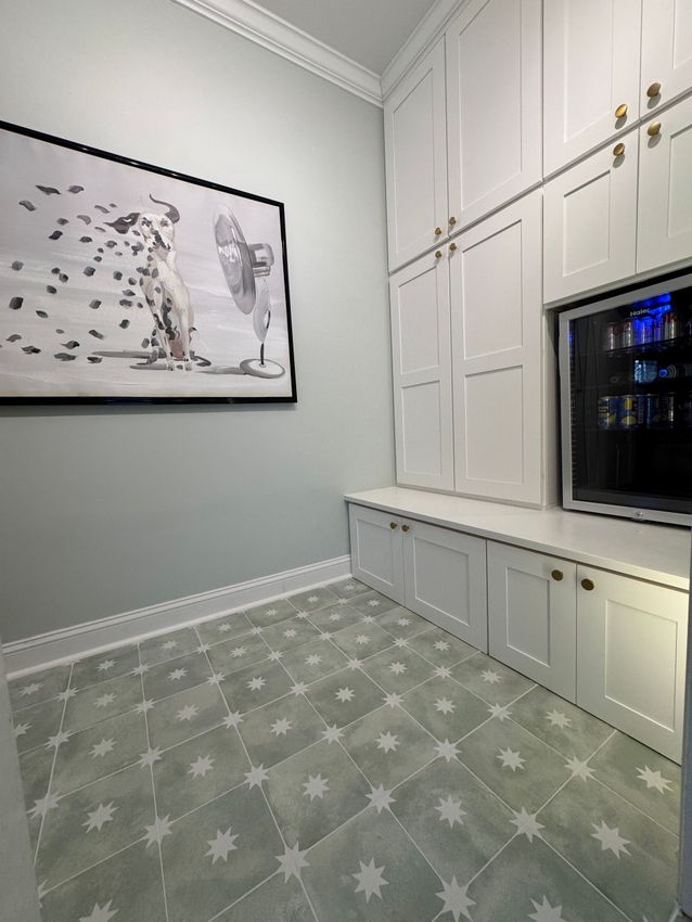 White built-in cabinets and bench along a wall in a bright room with patterned green carpet and framed art.