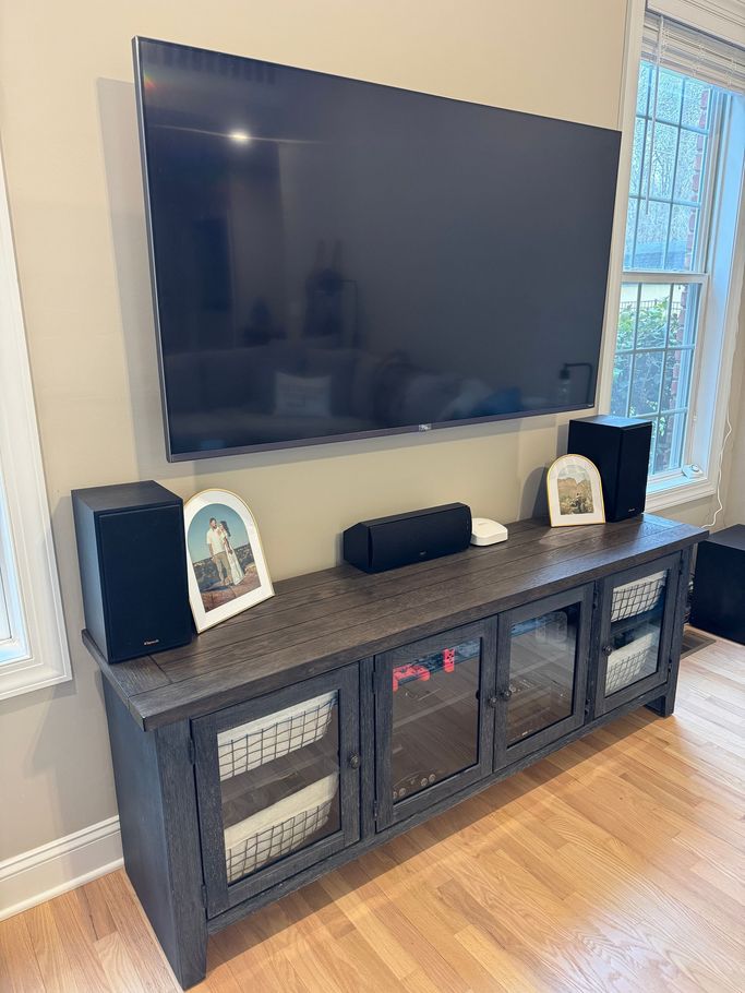 Living room TV mounted above dark wooden console with speakers and framed photos