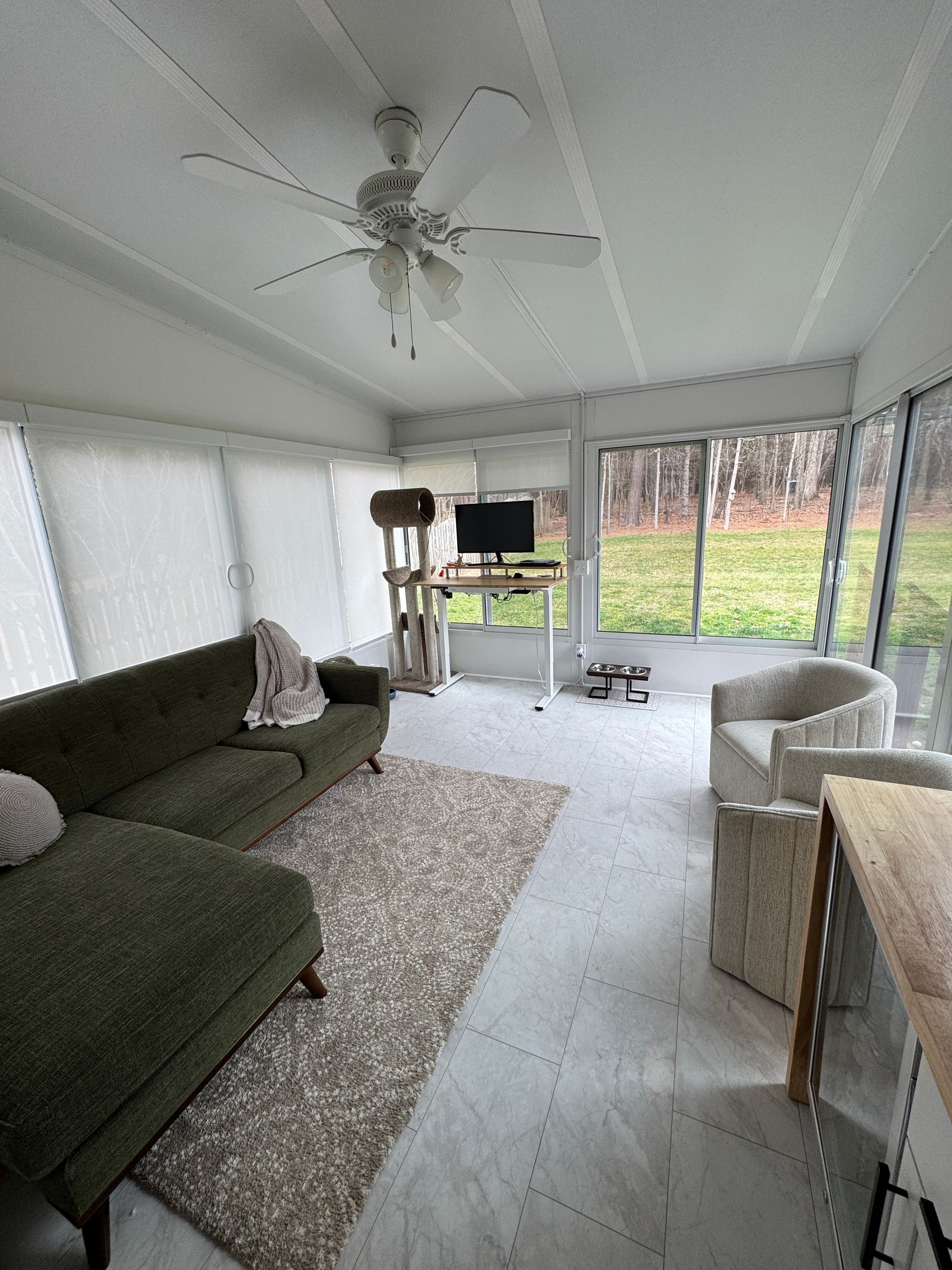 Sunroom with green sofa, white chairs, rug, ceiling fan, and view of a grassy yard