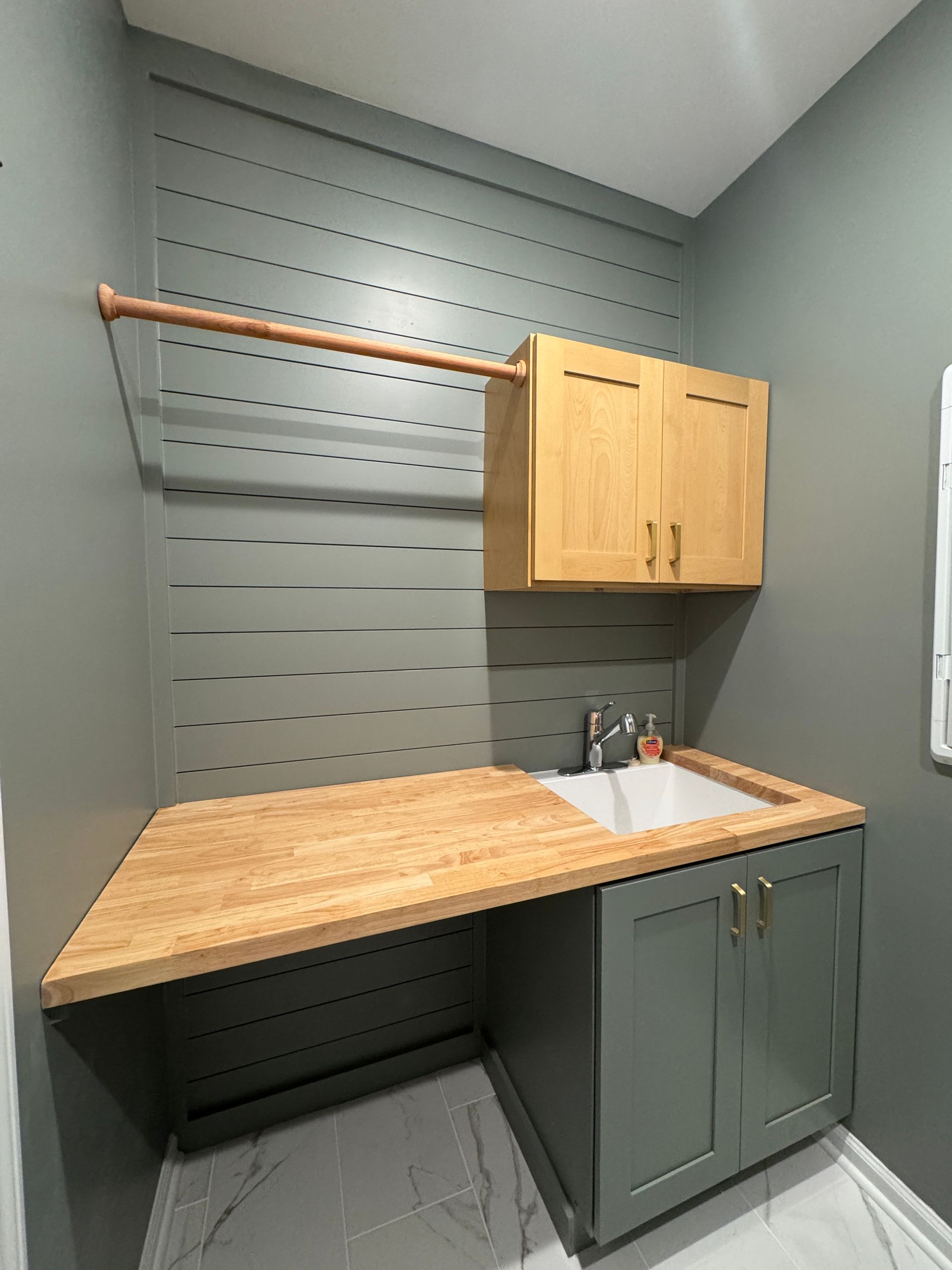 Small utility room with slatwall, wood countertop, sink, and wall cabinet in gray-green tones