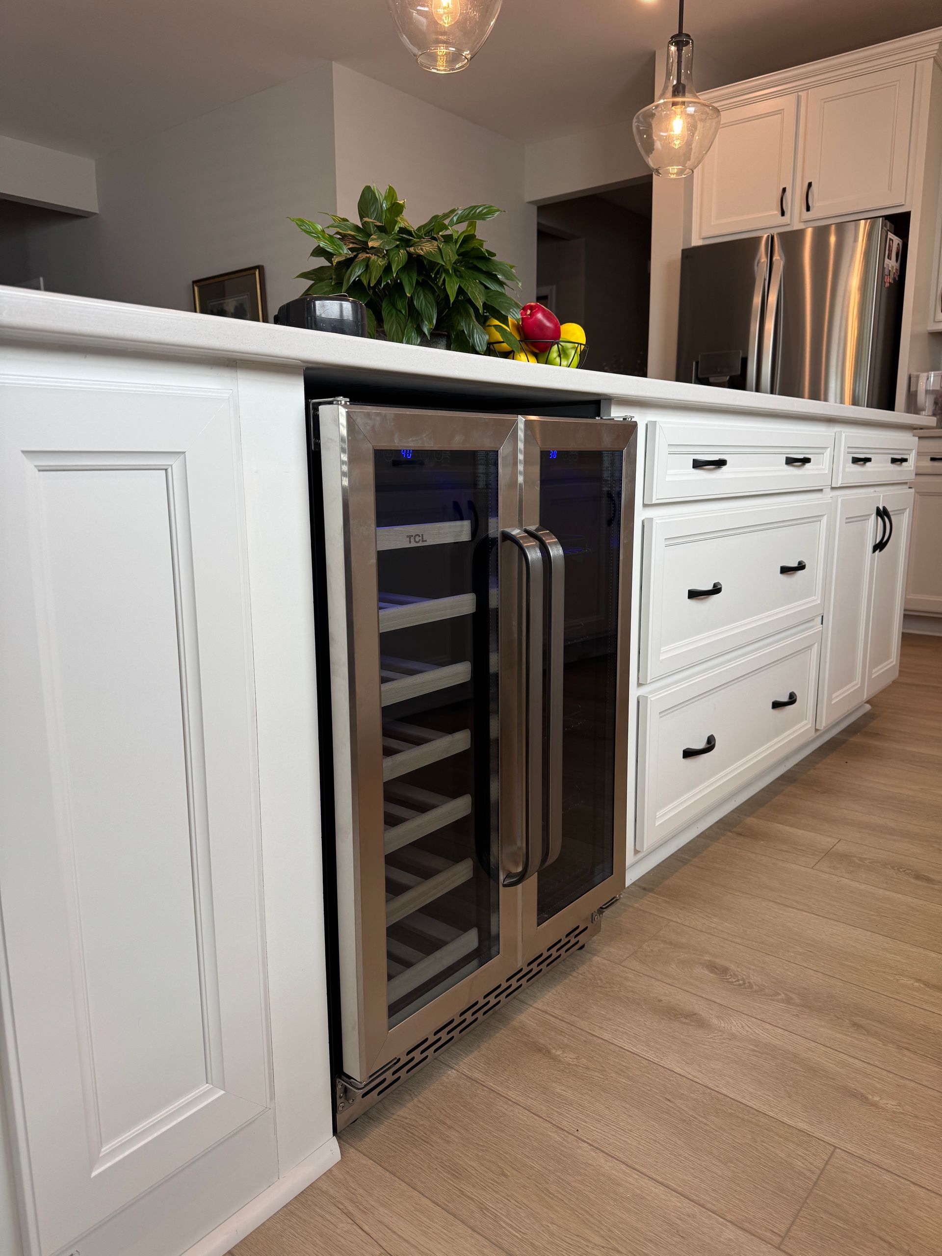 Modern kitchen with white cabinets, stainless wine cooler, black countertop, and stainless refrigerator in background
