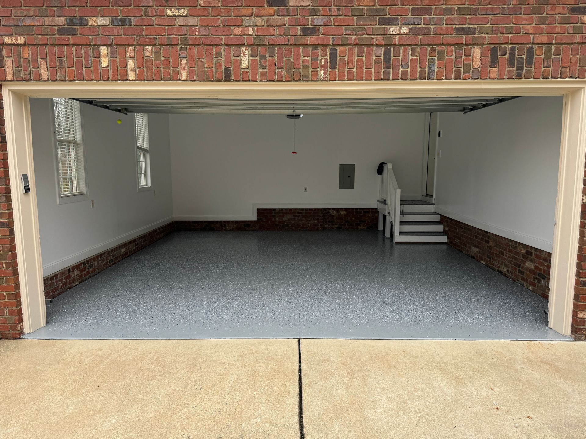 Open garage with gray floor, brick walls, and a small staircase at the back.