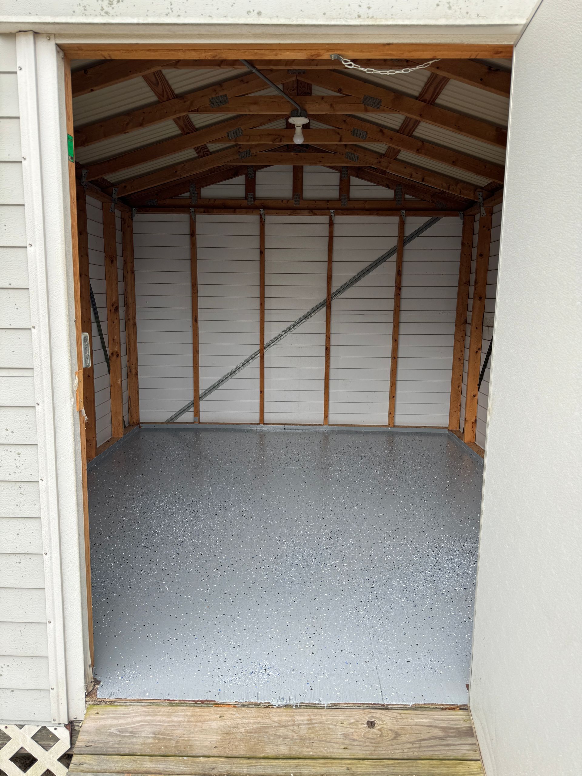 Open garage with gray epoxy floor and exposed wood roof framing.