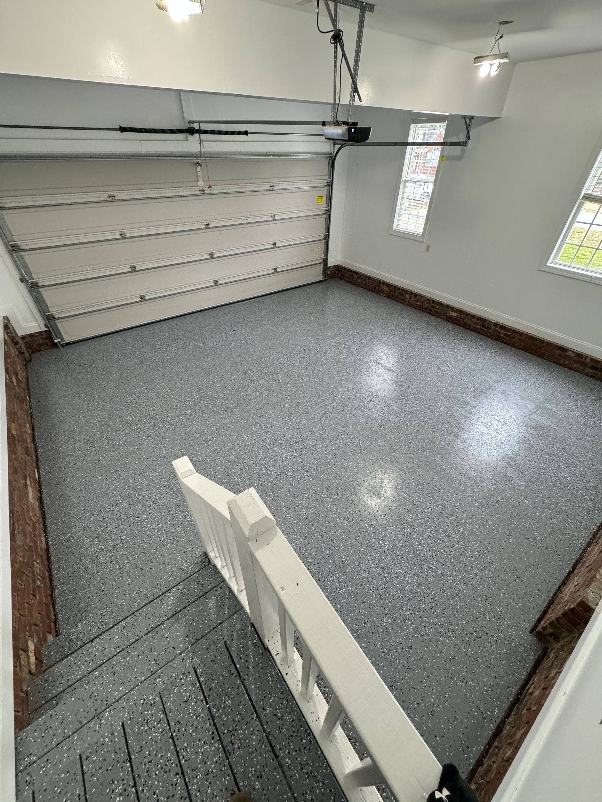 Empty garage with gray epoxy floor, white walls, and a closed sectional garage door.