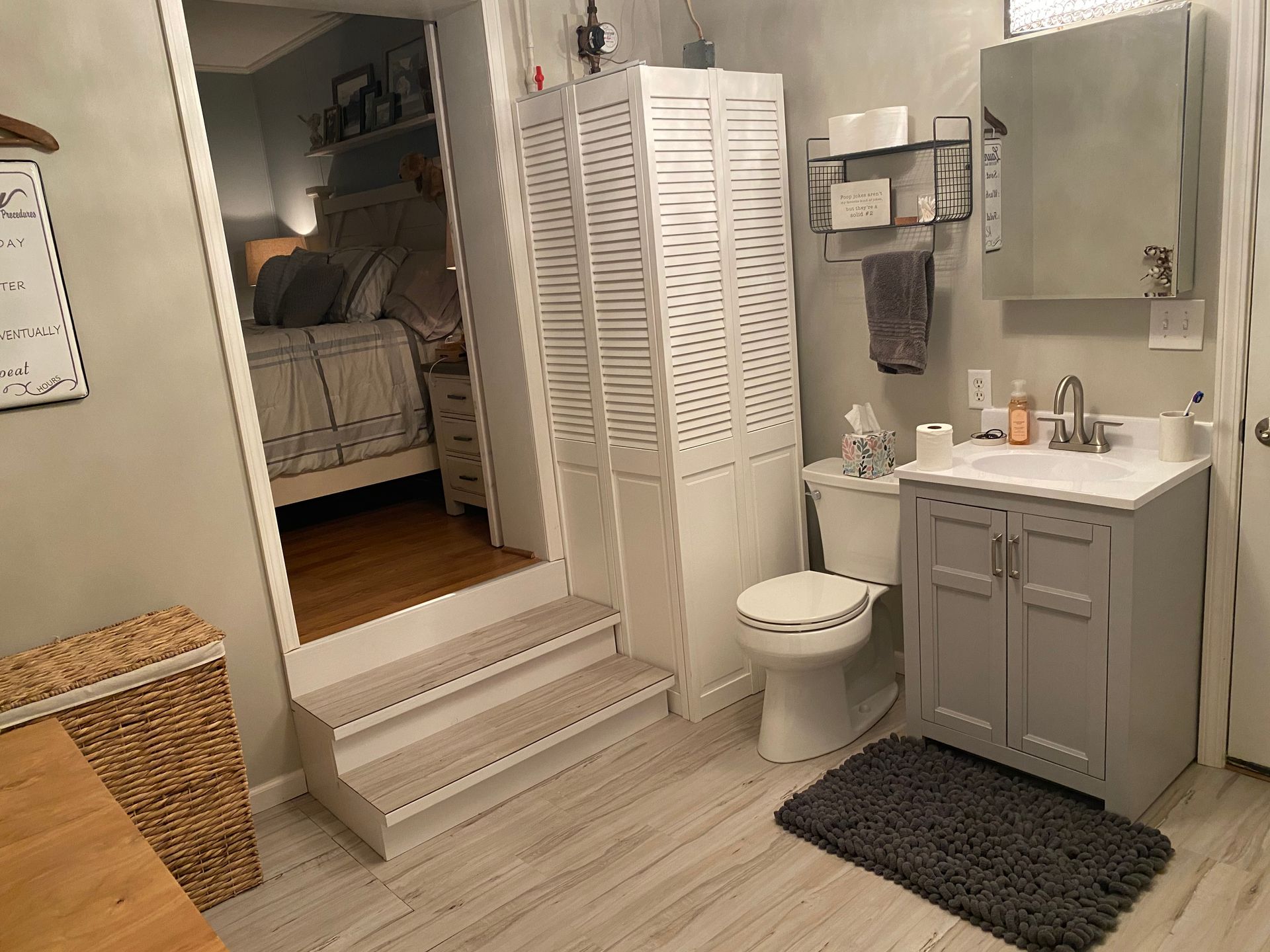 Small bathroom with white vanity, toilet, step-up tub/shower, and folding screen; bedroom visible through doorway