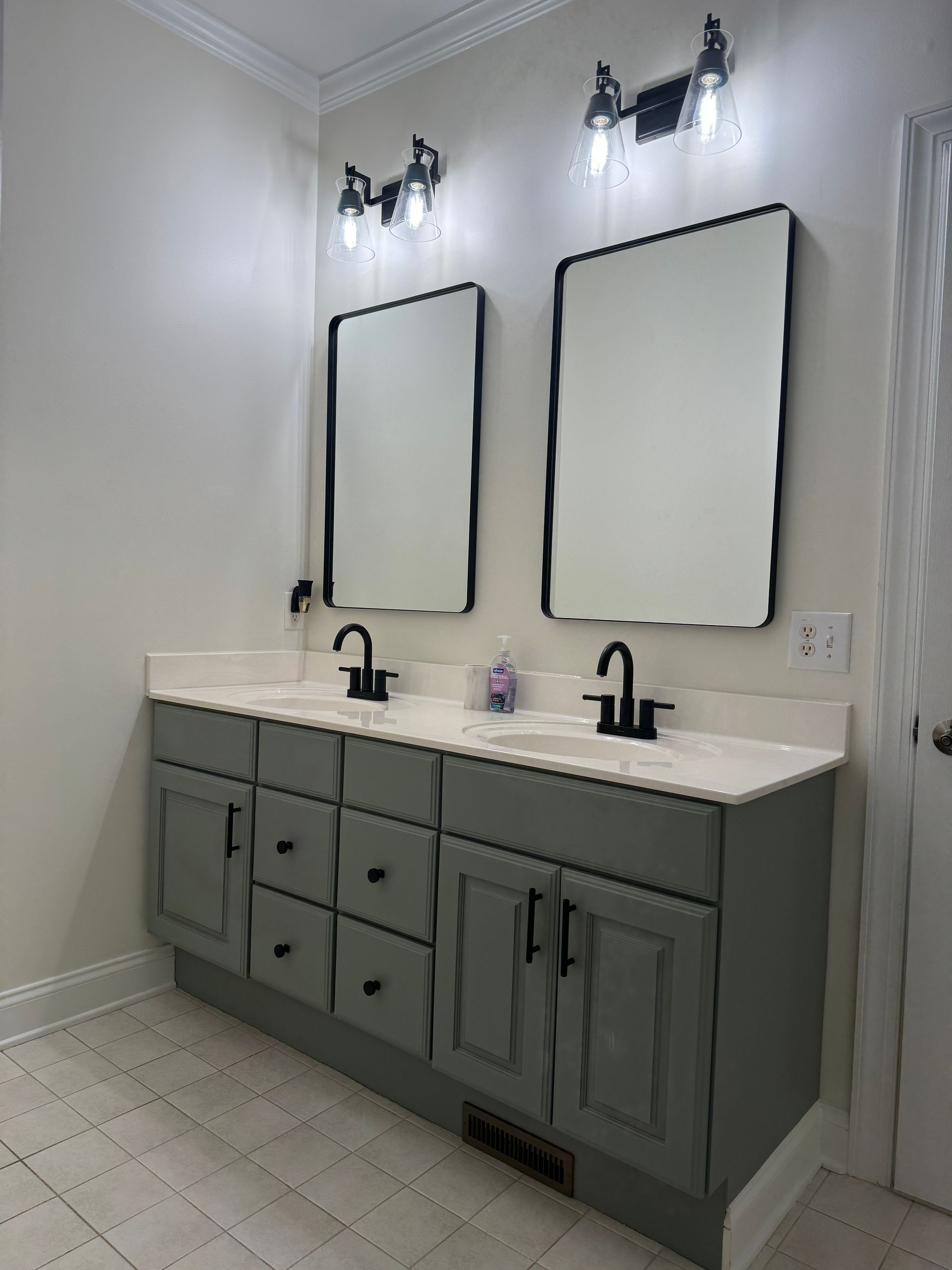 Modern double-sink bathroom vanity with green cabinets, white countertop, and wall mirrors under sconces.