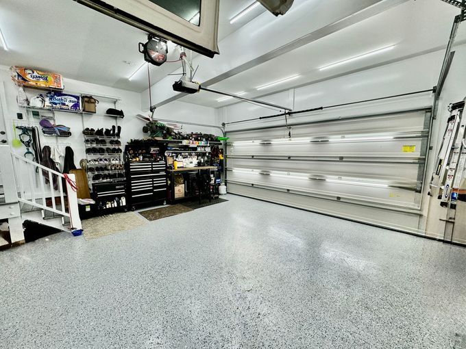 Bright two-car garage with white walls, speckled floor, overhead lights, and organized storage shelves.