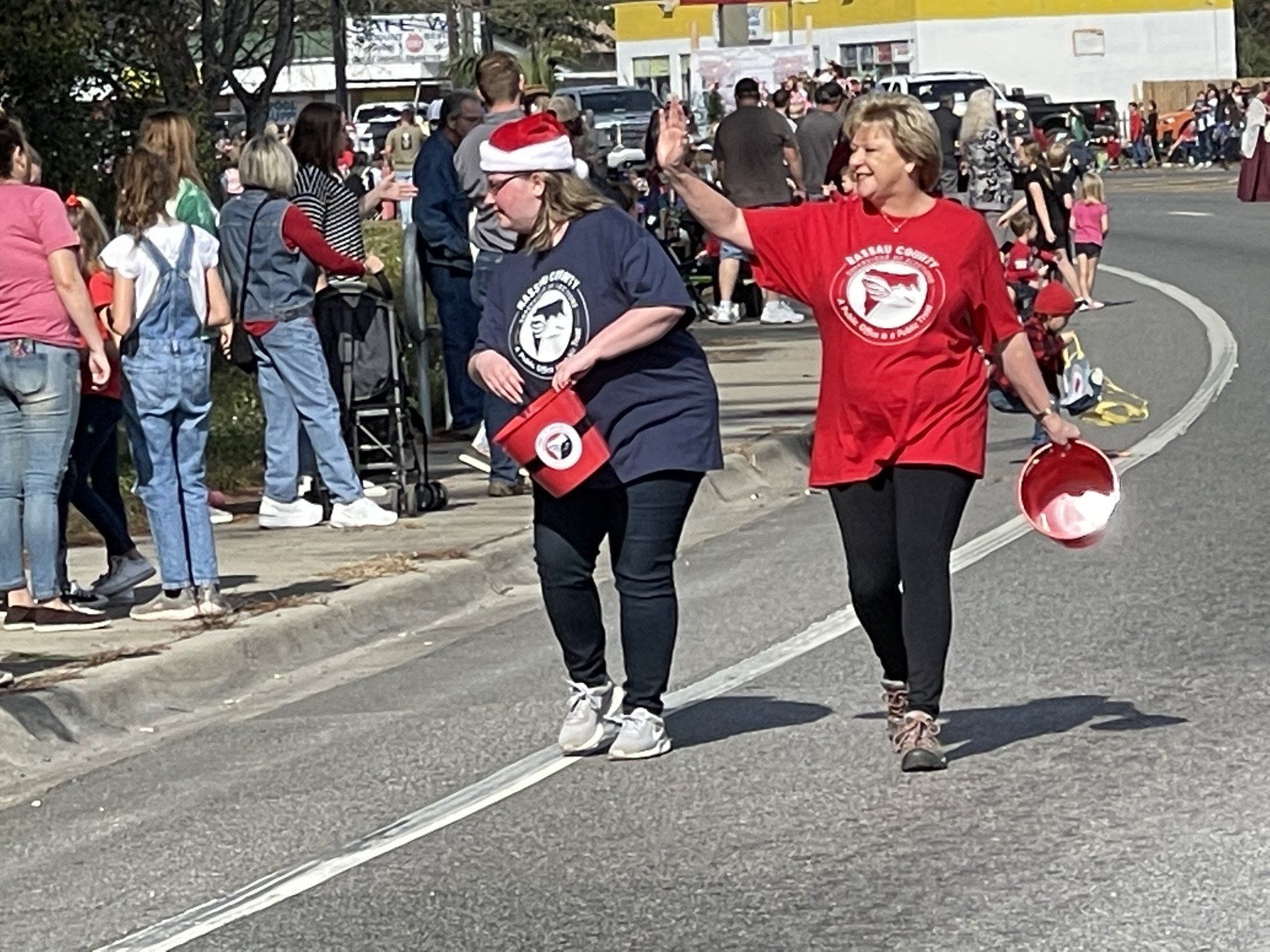 Two women wearing santa hats are walking down the street.