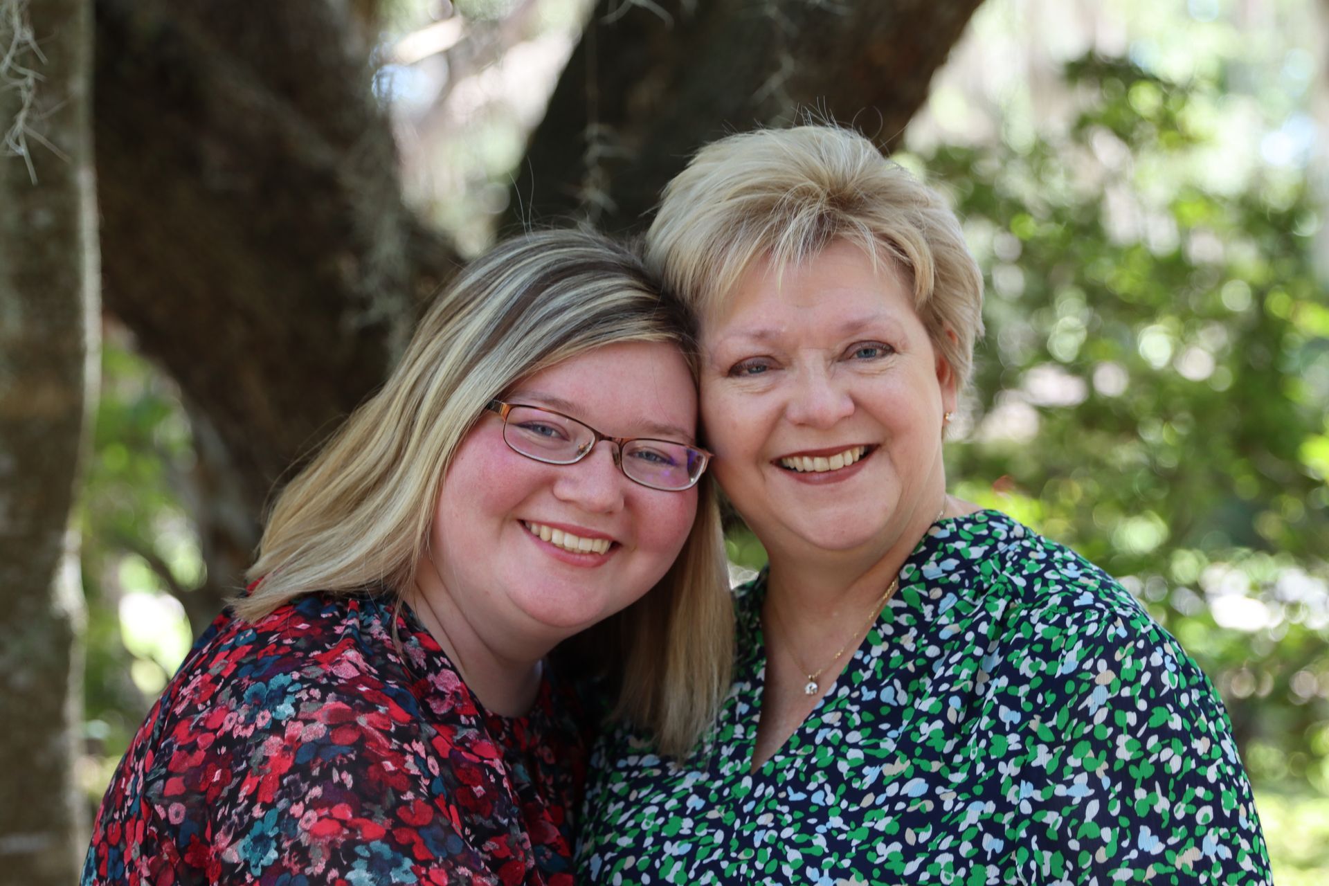 Two women are posing for a picture together in front of a tree.