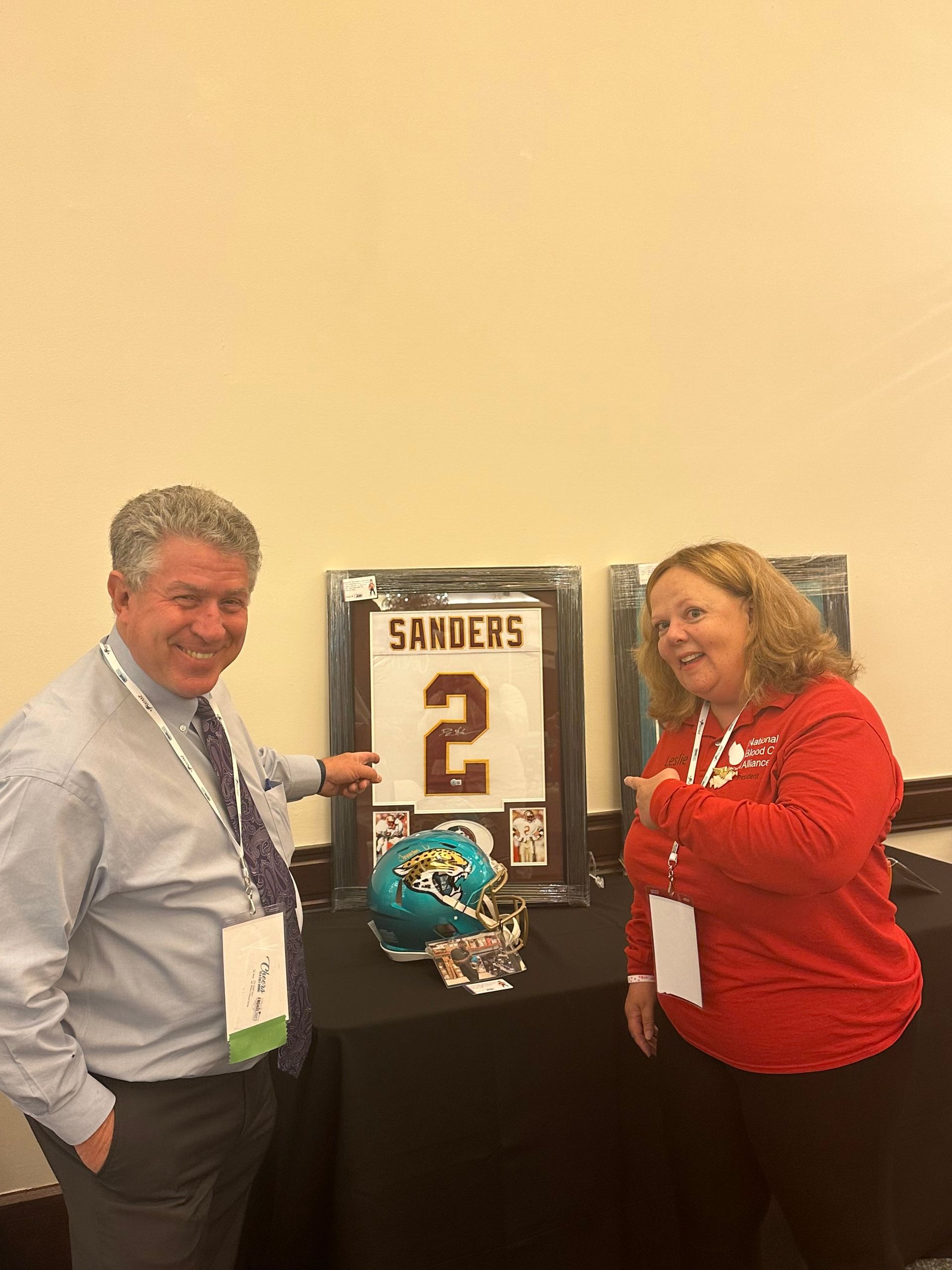 A man and a woman are standing next to each other in front of a framed football jersey.