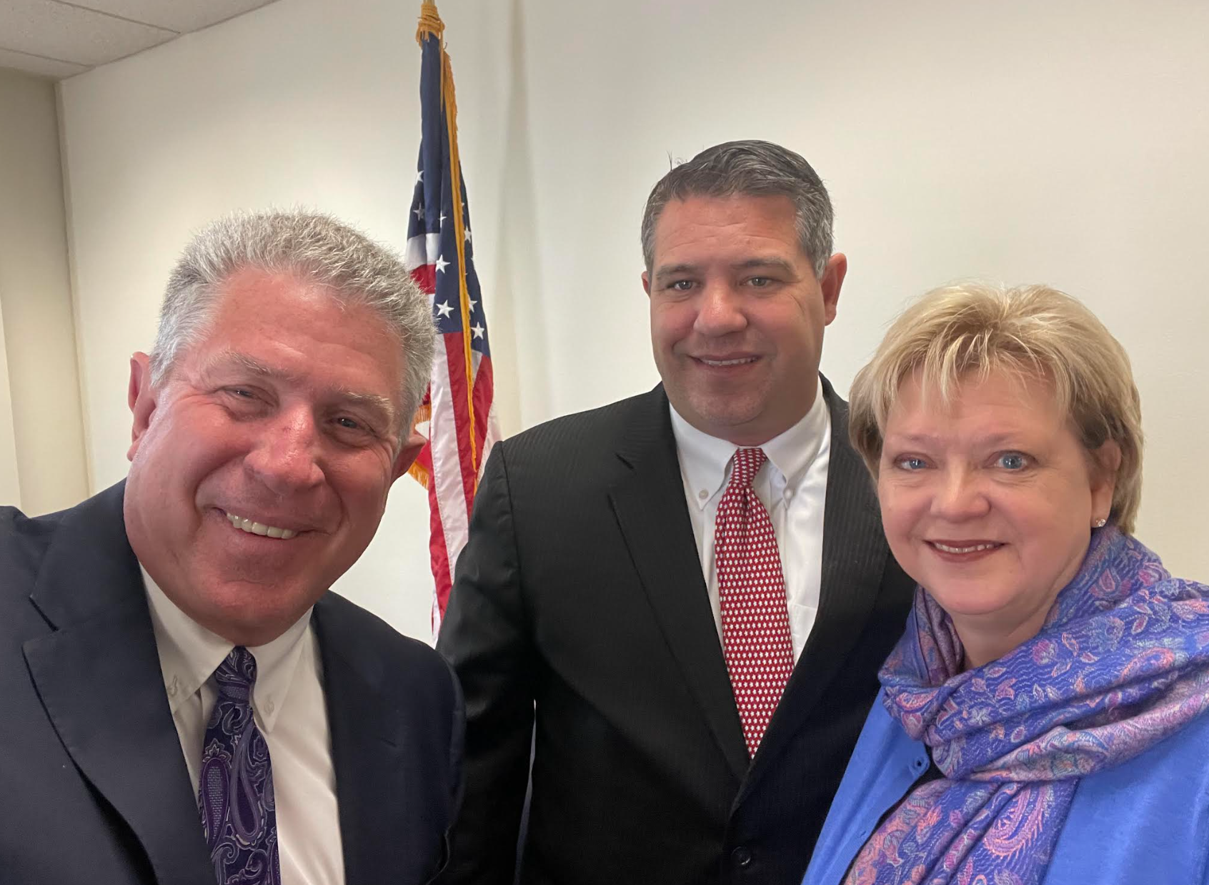 Two men and a woman are posing for a picture in front of an american flag.