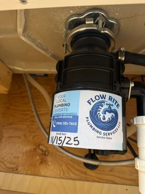 A black garbage disposal unit installed under a kitchen sink, featuring a service sticker marked 