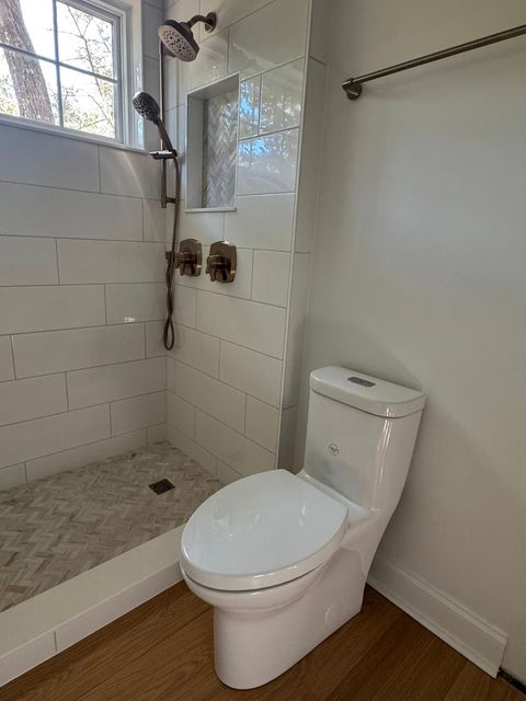 A white toilet sits in a small bathroom next to a glass-enclosed shower with white subway tiles and a wooden floor.