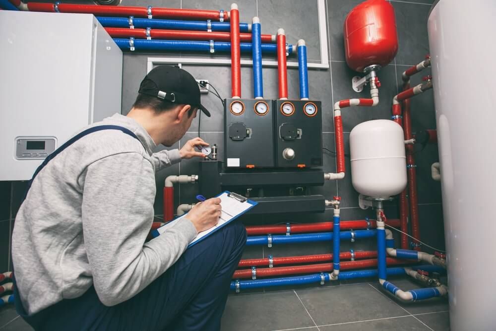 Man Kneeling Down in A Room with Pipes and Writing on A Clipboard — Professional Plumber in Toowoomba